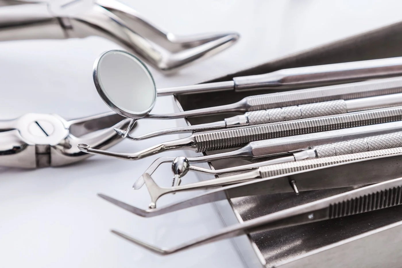 Close-up of dental tools on a tray, including a mirror, probes, and forceps.