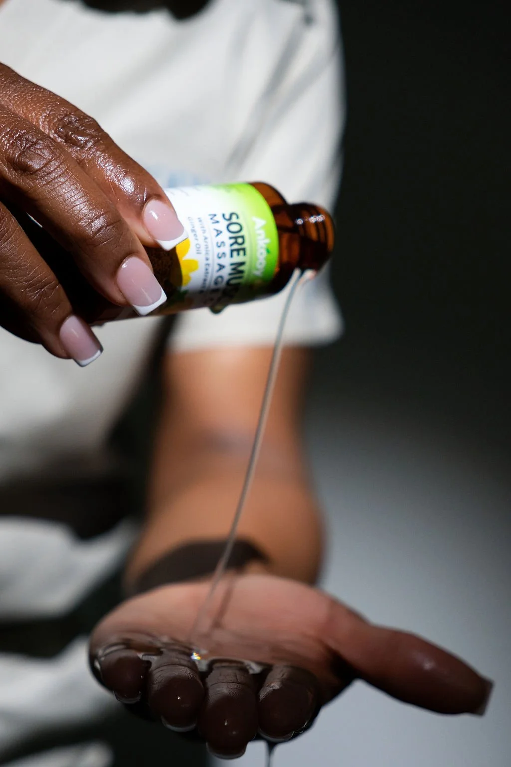 Person pouring massage oil into their hand from a brown bottle labeled "Sore Muscle Massage."