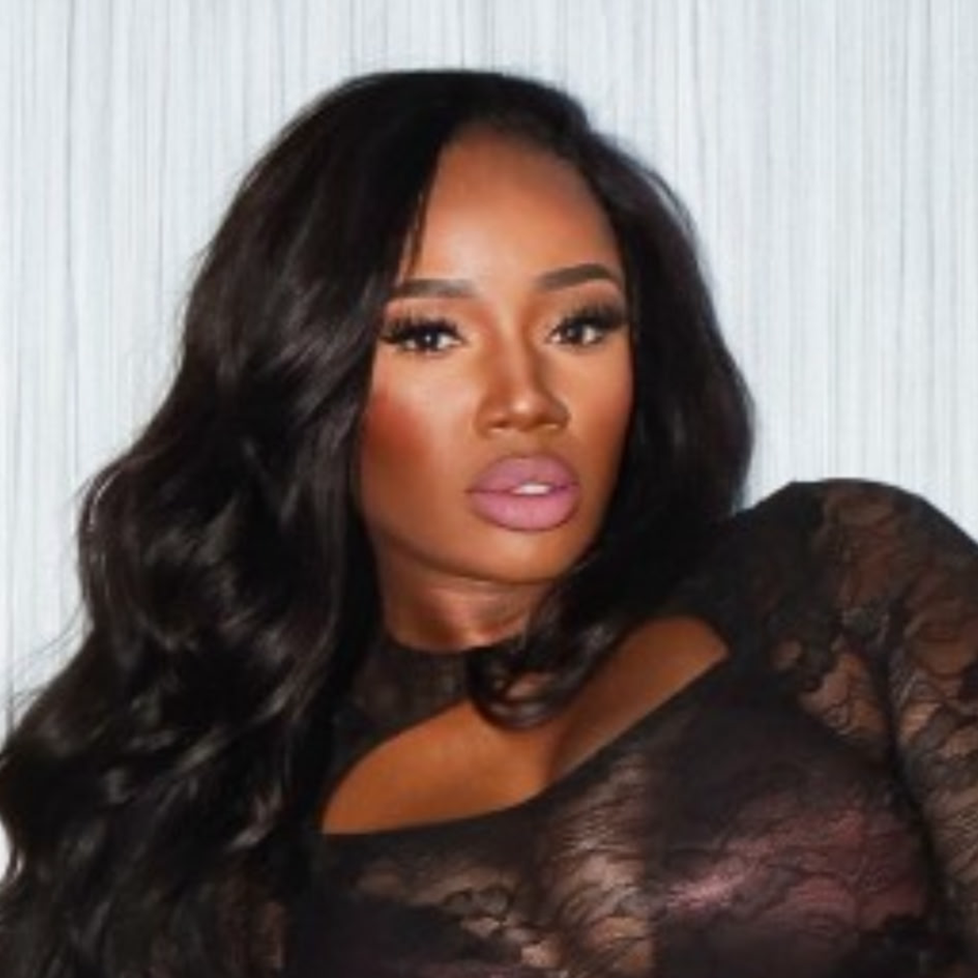 A woman with long, wavy black hair wearing a black lace outfit.