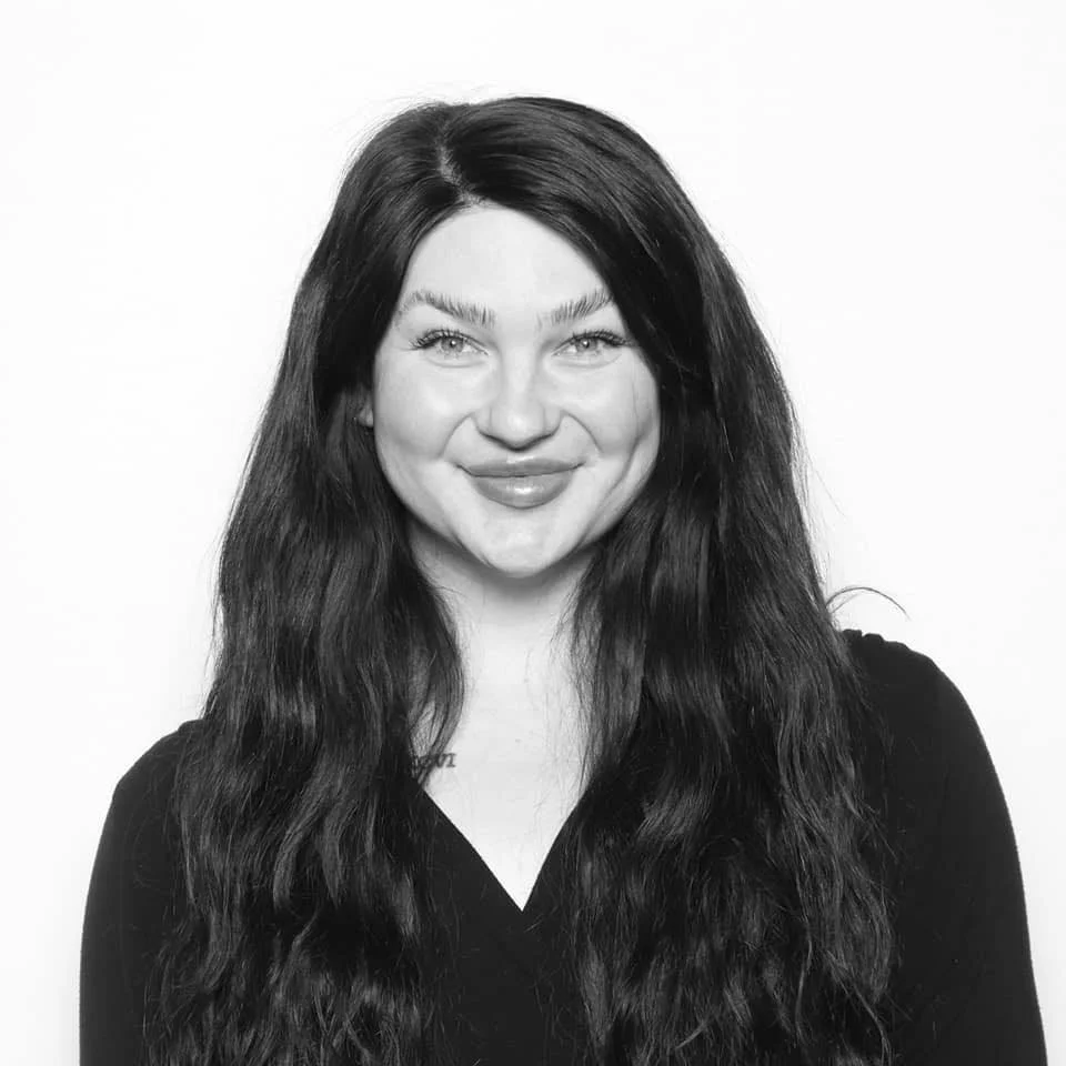 Black and white photo of a woman with long dark hair and a bright smile, wearing a black top against a plain background.