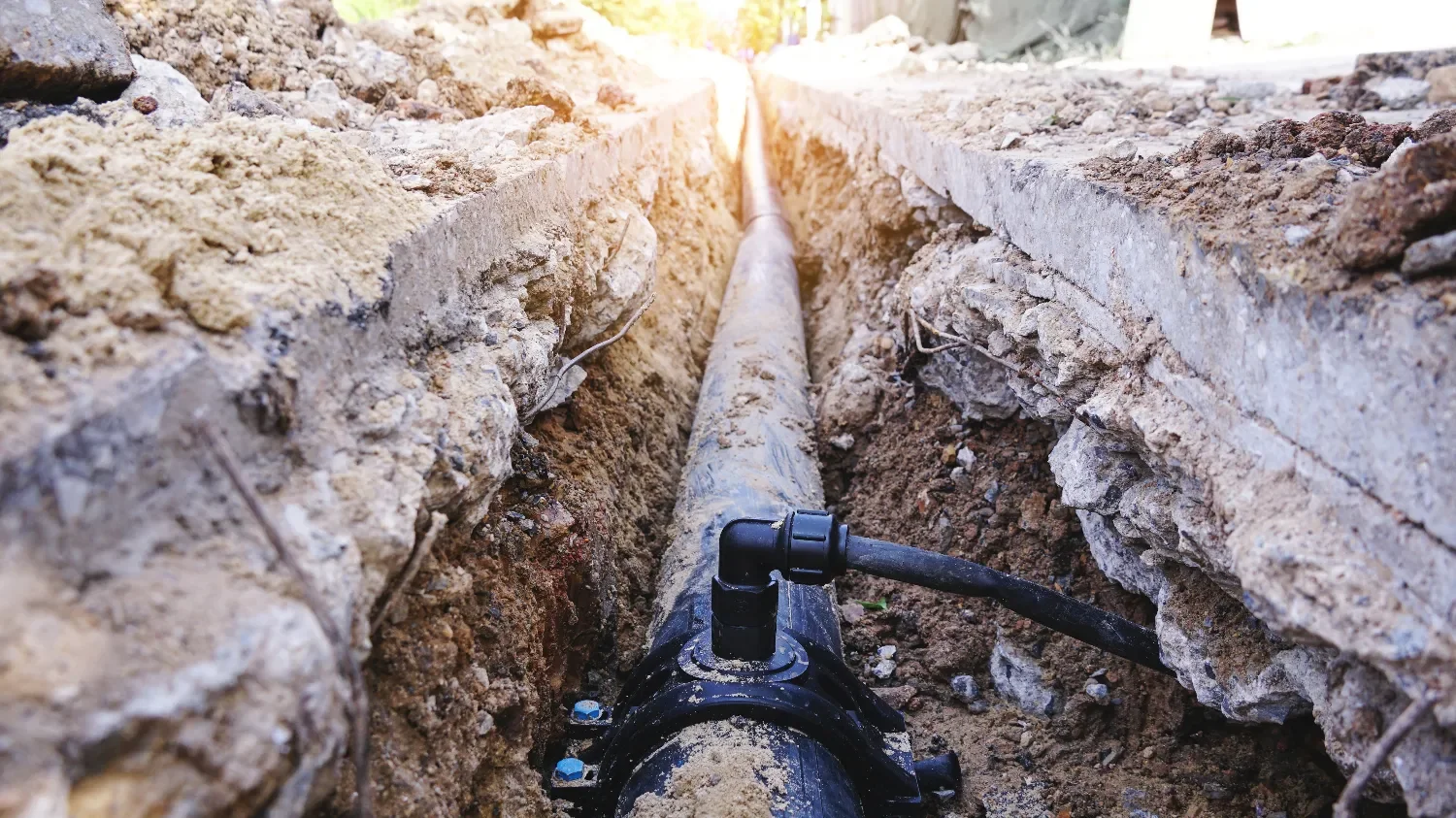 A long pipe running through a trench under construction, with soil and rubble on either side.