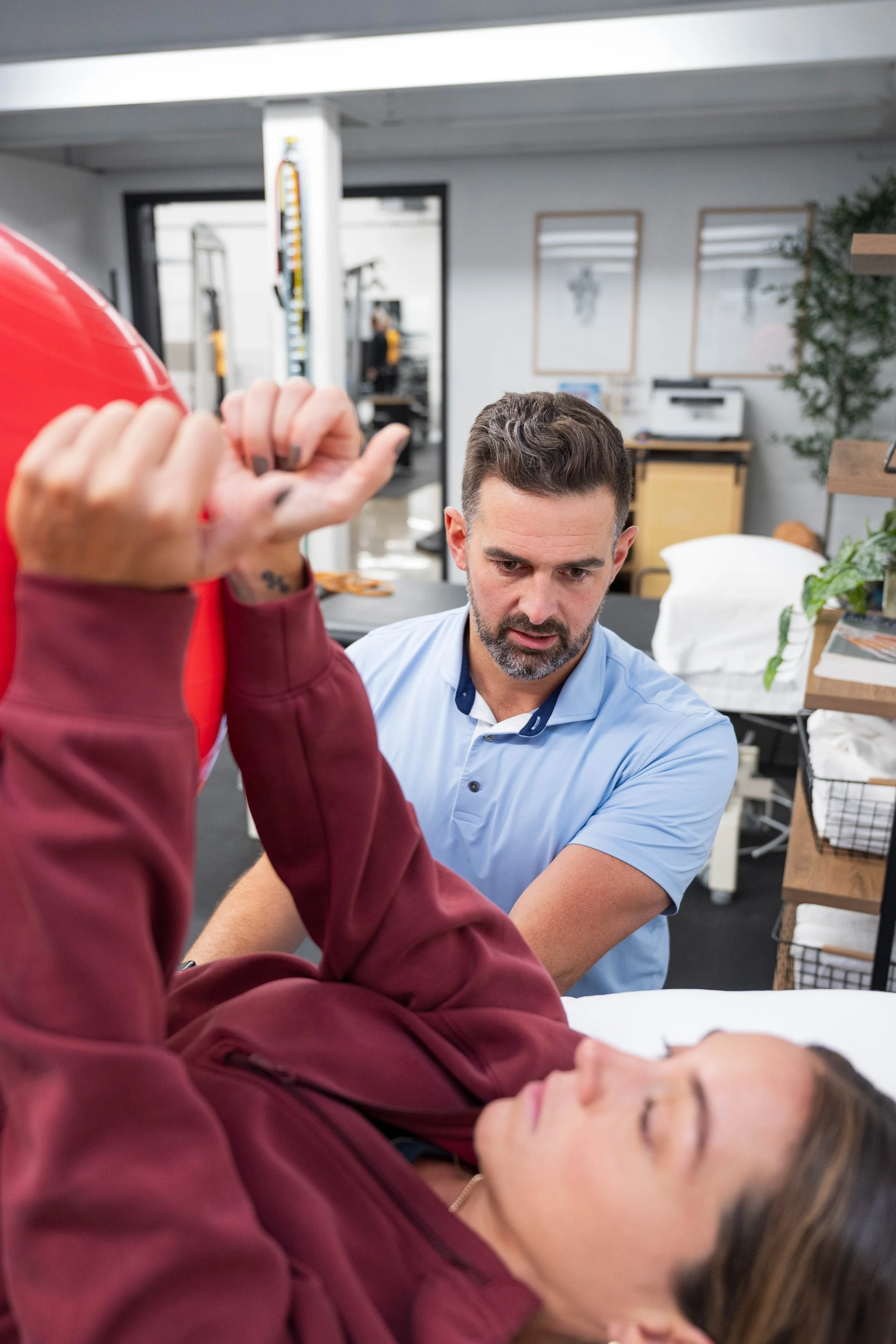 Man in a light blue shirt examines a woman's injured arm in a bright medical clinic.