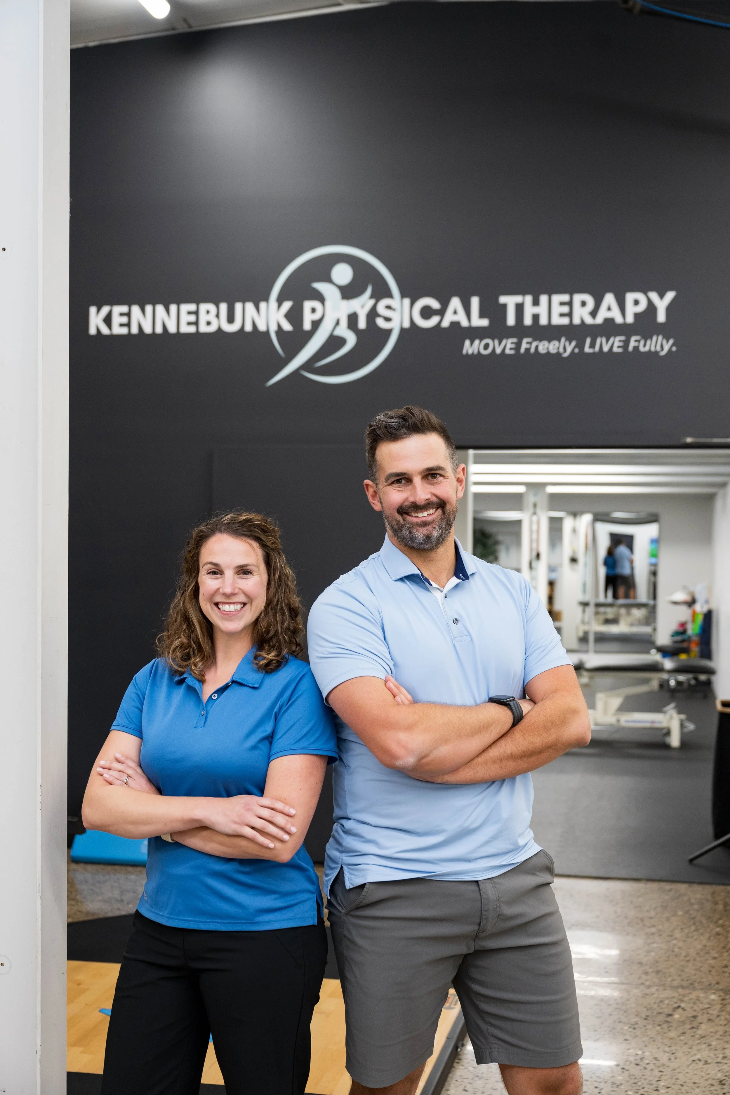 Two smiling physical therapists pose with crossed arms inside Kennebunk Physical Therapy.