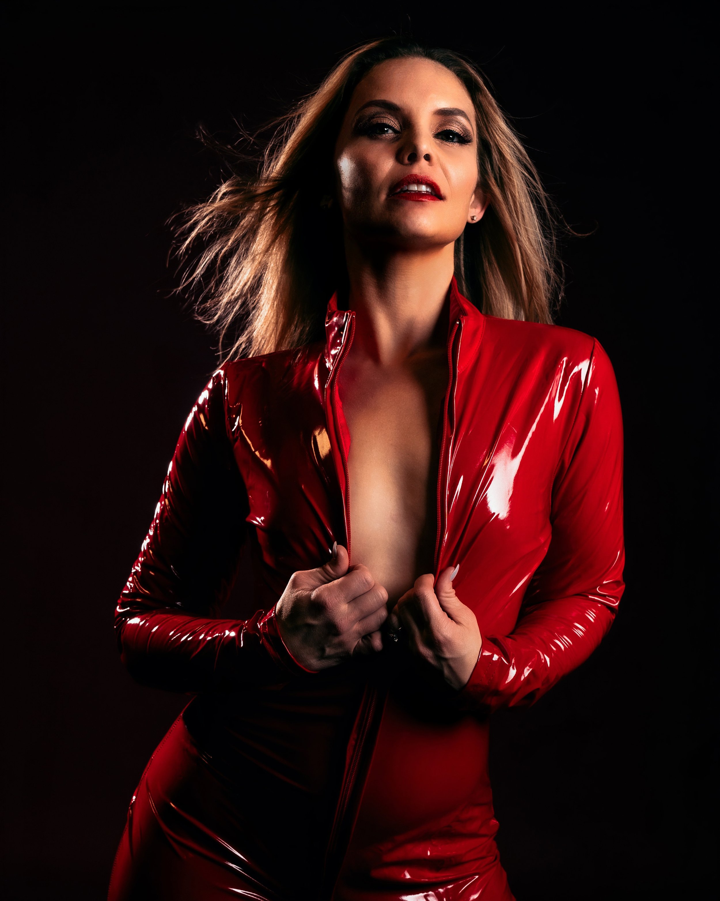 A woman with long hair wearing a shiny red jacket, posing against a dark background.