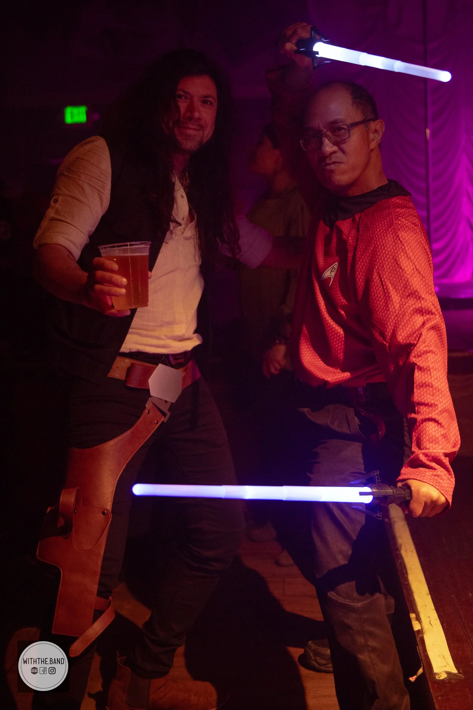 Two men dressed as characters from Star Wars, holding blue lightsabers, posing for a photo at a costume event or party.