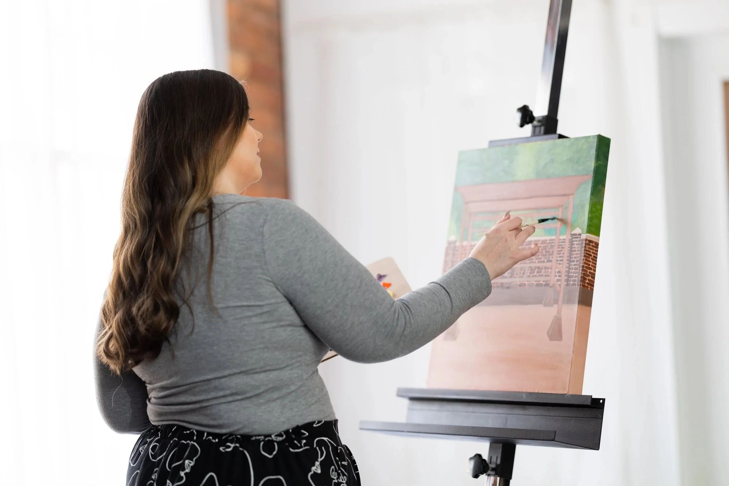 Woman painting on a canvas in a bright room with an easel.