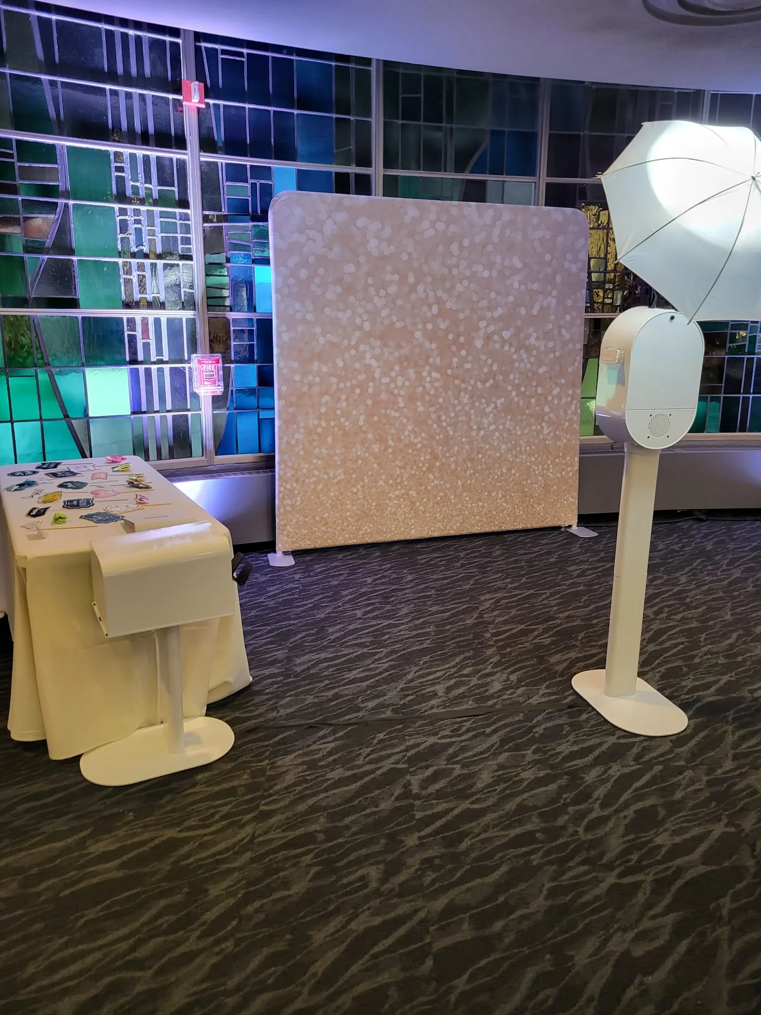 Photo booth setup with a speckled backdrop, camera stand, and lighting in front of a glass panel wall.