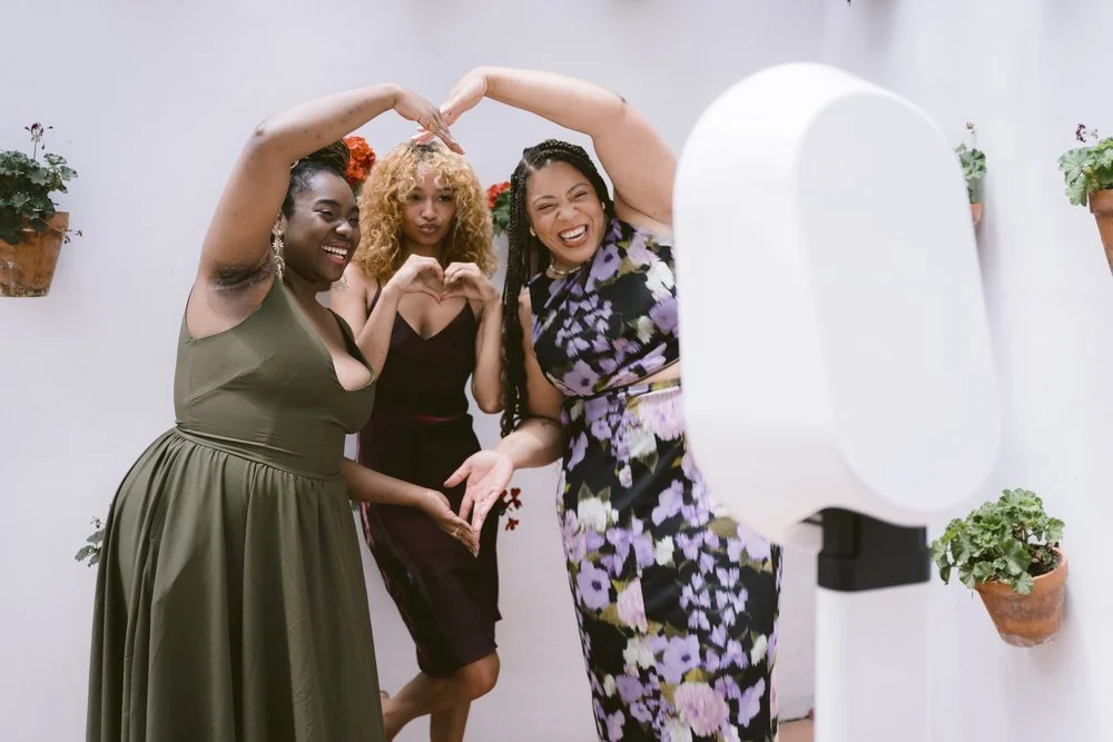 Three women posing joyfully for a photo booth, forming a heart shape with their hands.