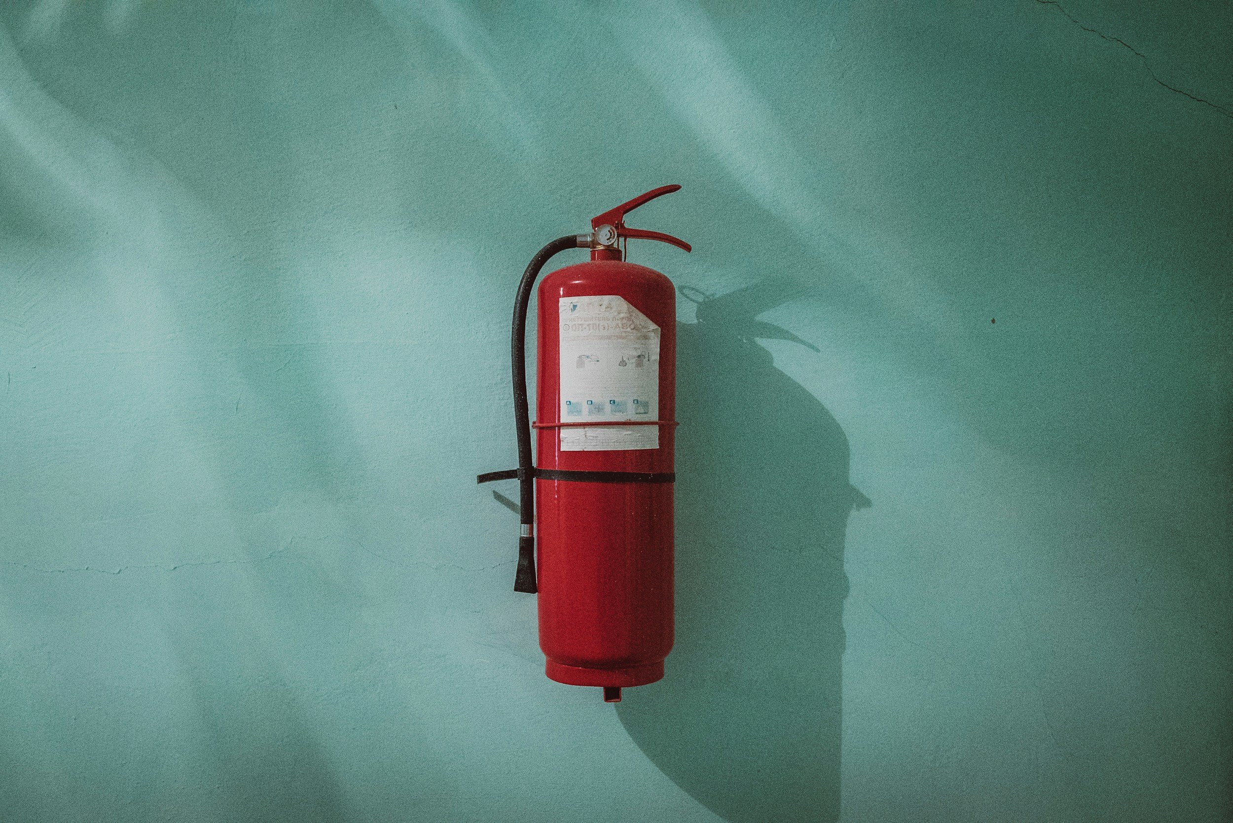 Red fire extinguisher mounted on a teal wall