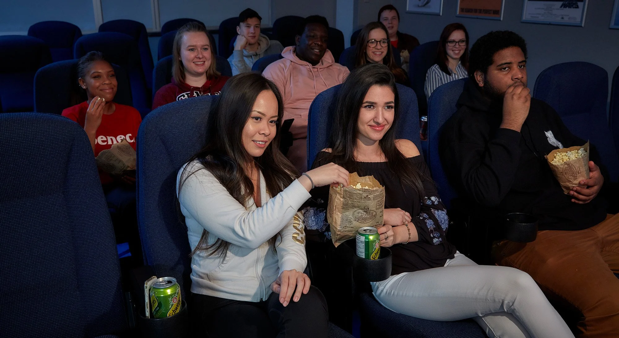 A group of people sitting in a movie theater, watching a film, with some eating popcorn and drinks.