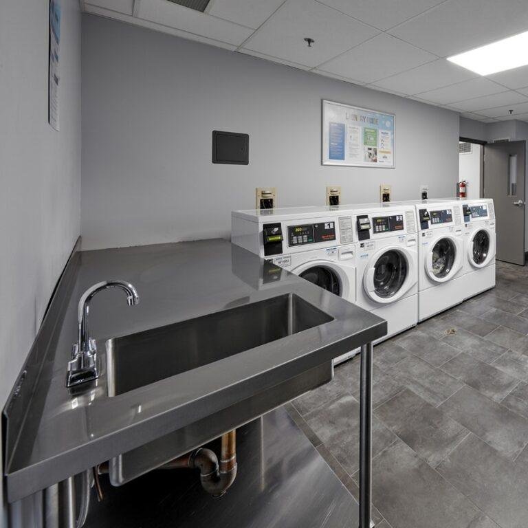 Laundry room with four washing machines, a stainless steel sink, and a wall-mounted informational poster.
