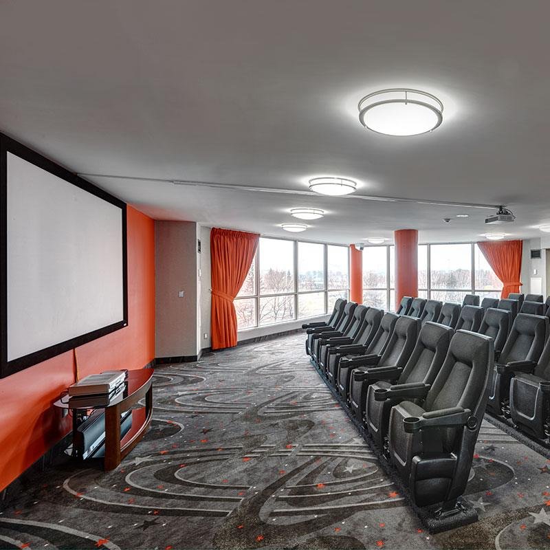 Empty movie theater with gray seats, large screens, and windows with orange curtains.
