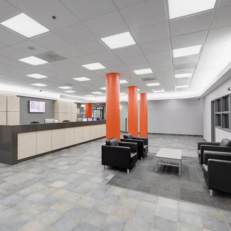 Lobbe with black armchairs, white coffee table, orange columns, and a reception desk with TV screens
