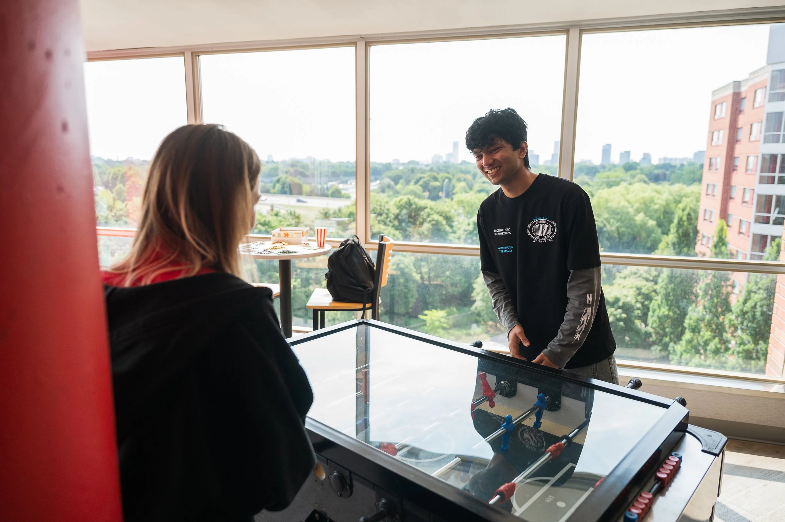 A young man sitting at a desk with an open book, a tablet, and a desk lamp in a bedroom or study area.
