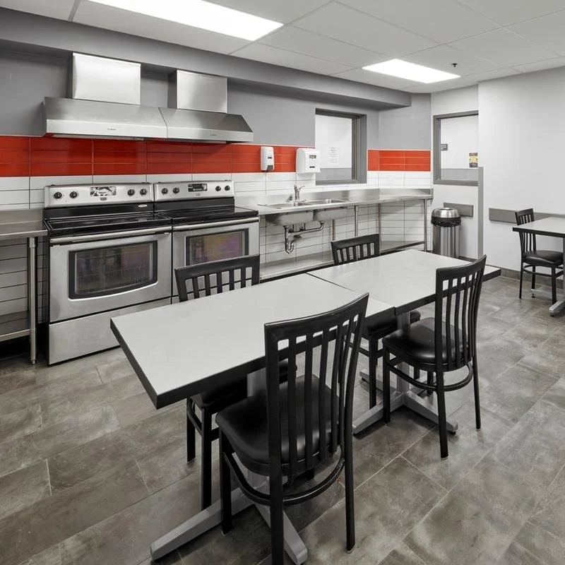 A kitchen with stainless steel appliances, a white and red tiled wall, and black chairs around a white table.
