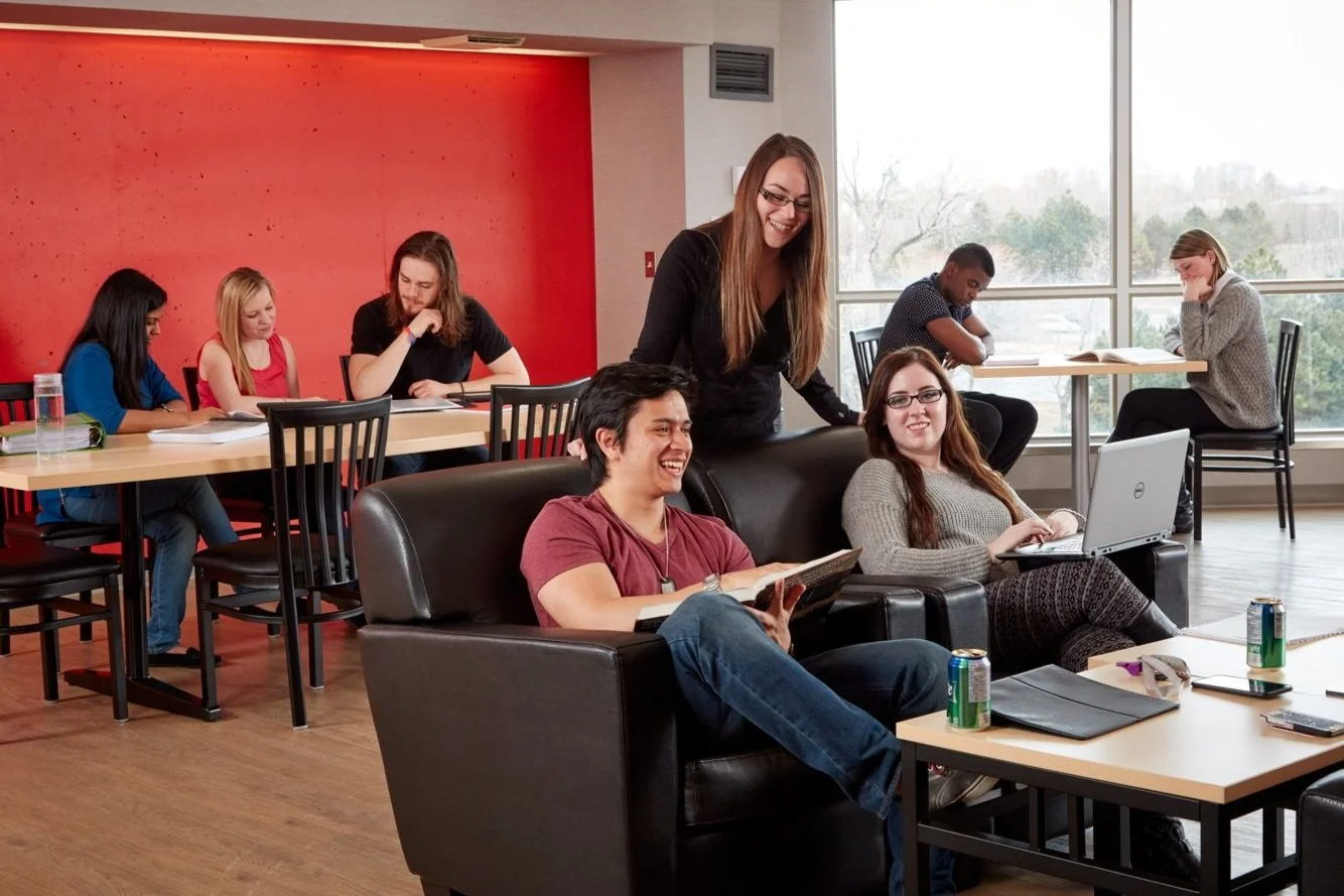 A diverse group of young adults in a casual, well-lit room with large windows.