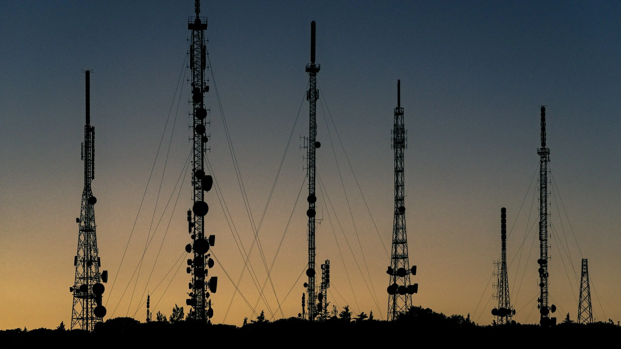 Silhouetted communication towers at sunset against a clear sky.