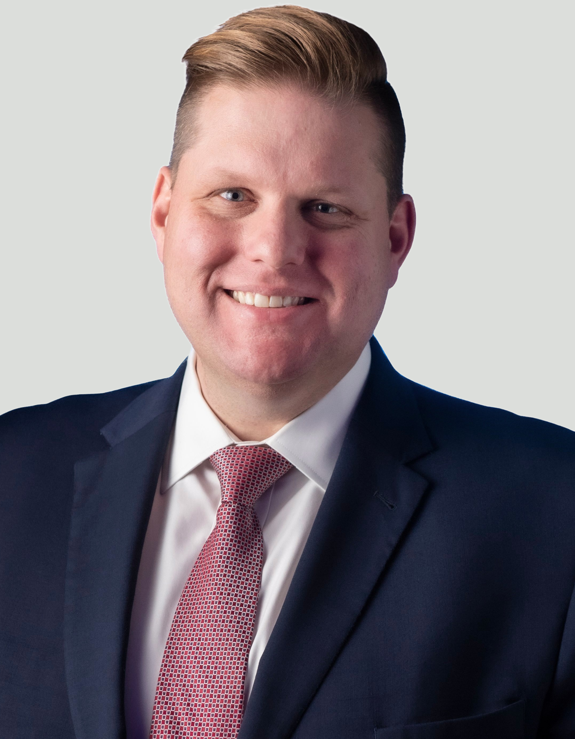Smiling man in a suit and tie against a light gray background.
