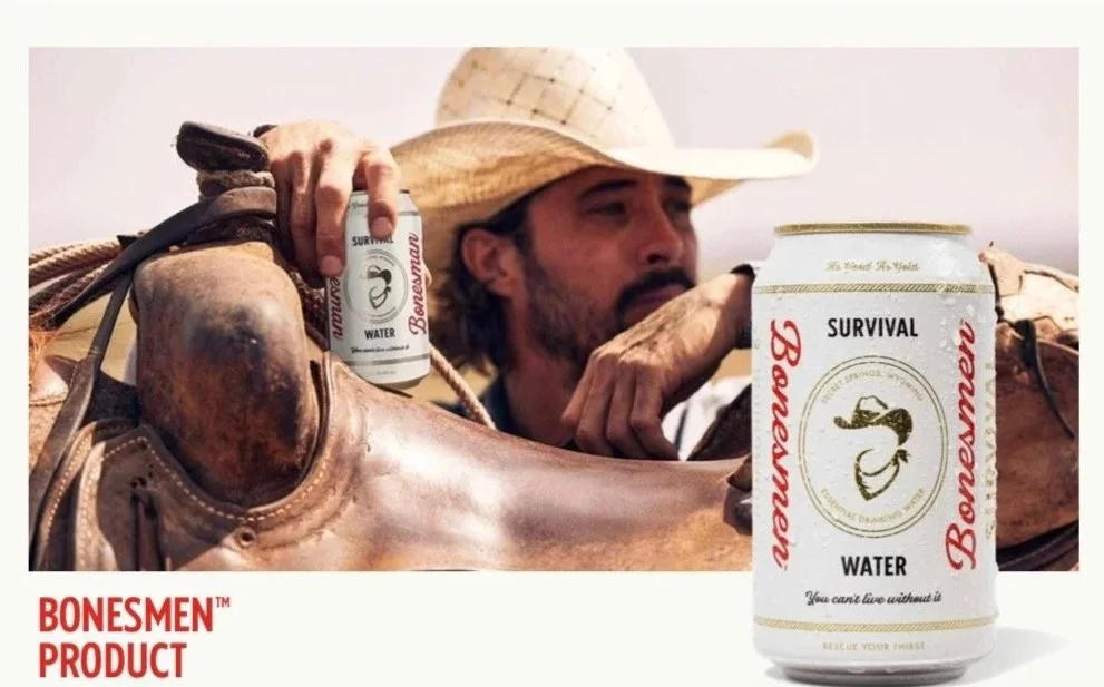 A man wearing a cowboy hat rests his arm on a saddle, holding a can of Bonesmen survival water in a desert setting with a clear sky.