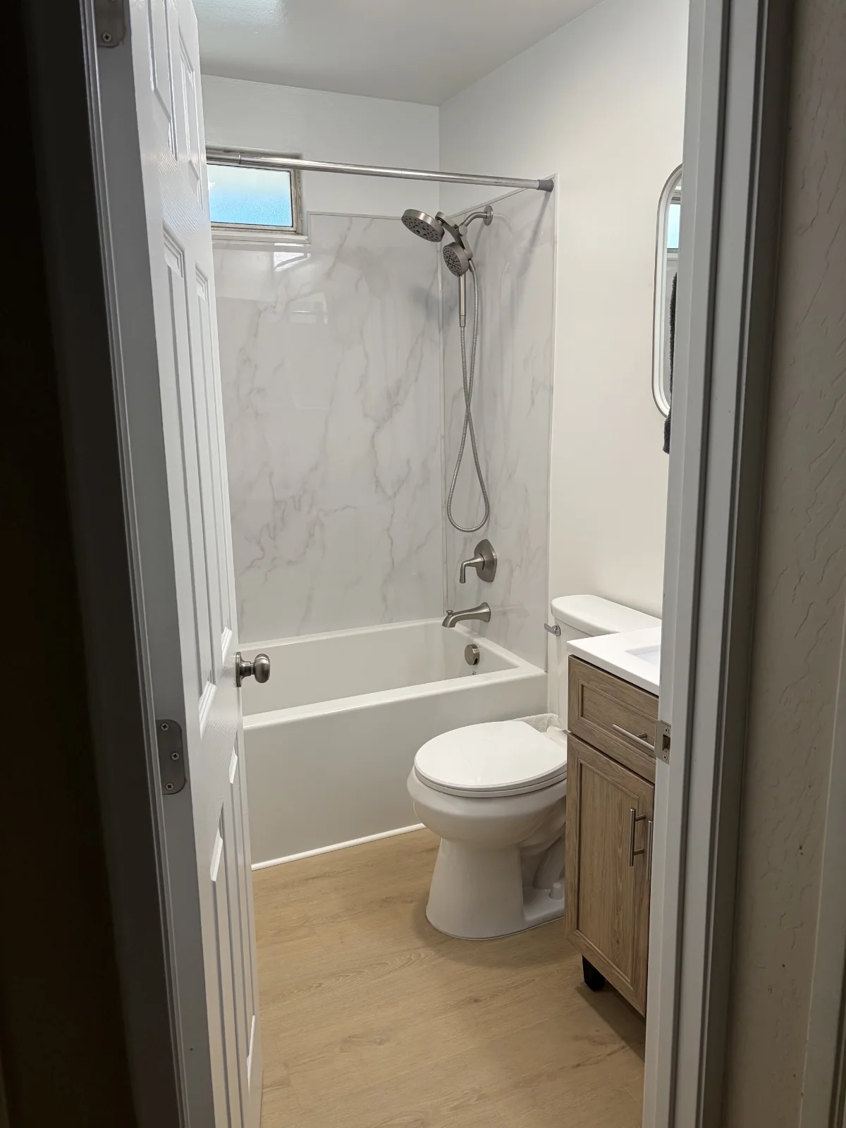 Remodeled bathroom with wood-grain vanity, white tub and marble-look wall surround in Redding