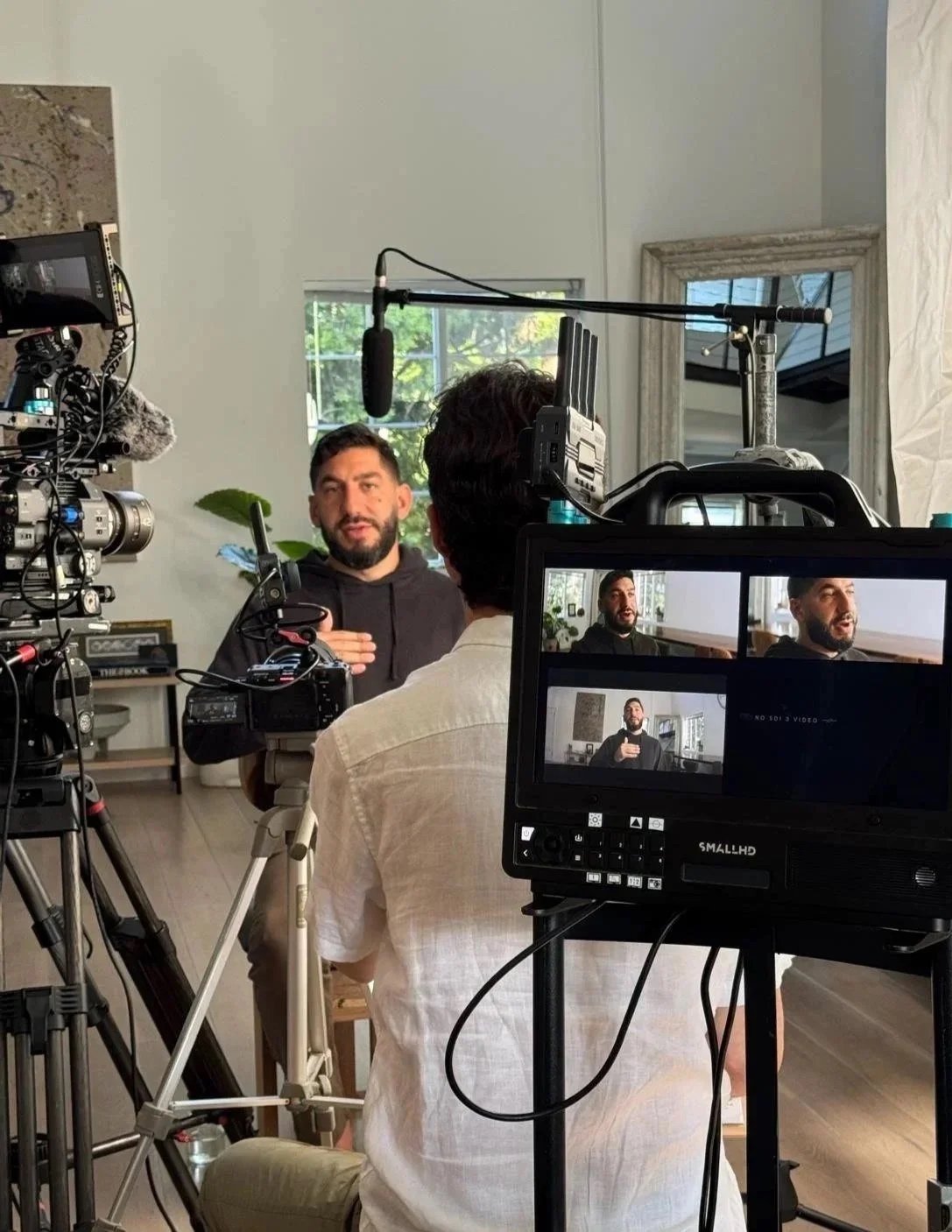 Film crew filming interview in a home setting with a man speaking, camera and monitoring equipment visible.