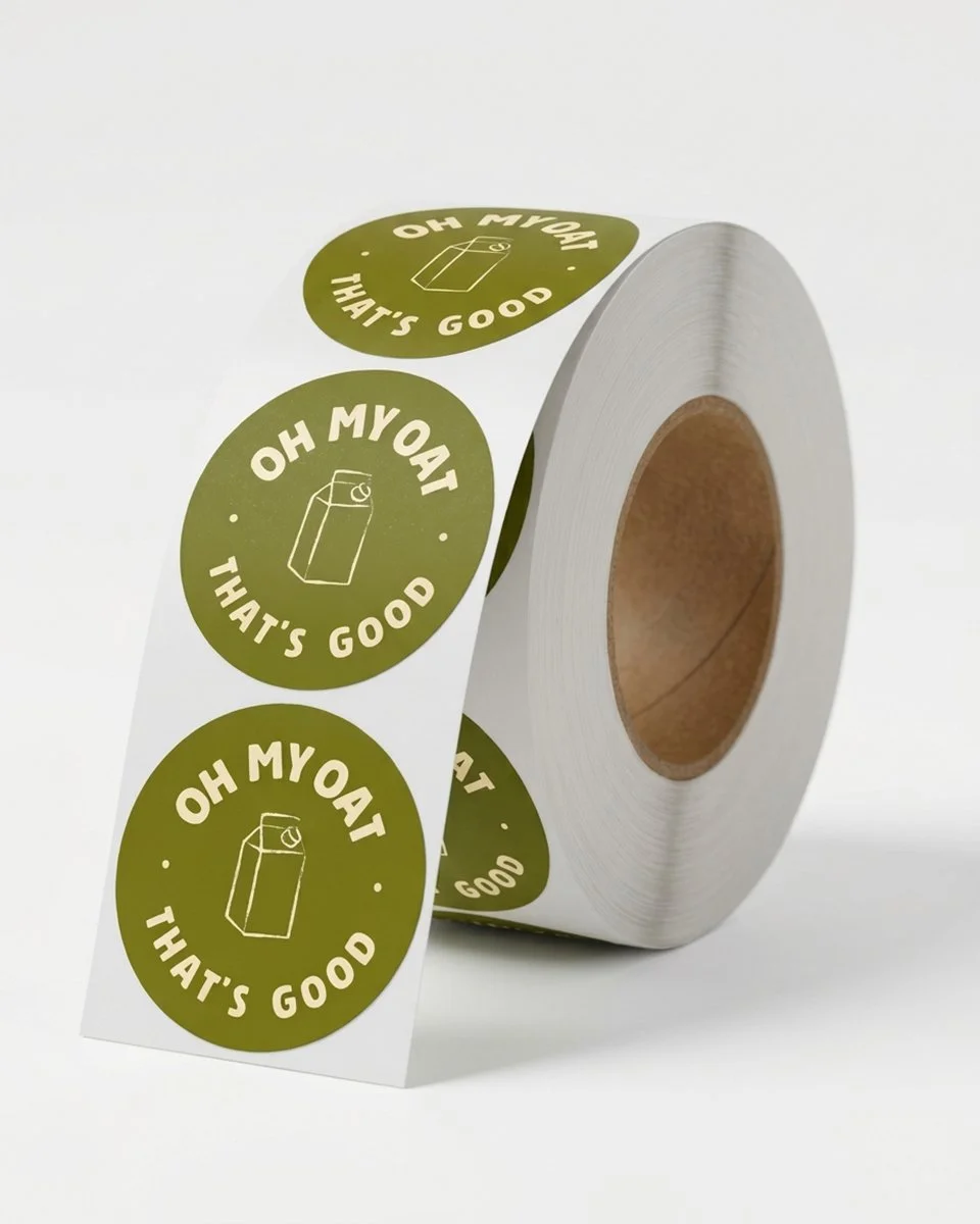 Roll label of green circular stickers reading “OH MY OAT THAT’S GOOD,” featuring an oat milk carton illustration.