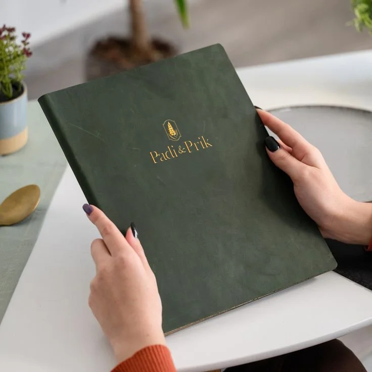 Hands holding a green leather folder featuring a Creative design, Menu cover with a gold foil Padi & Prik logo.