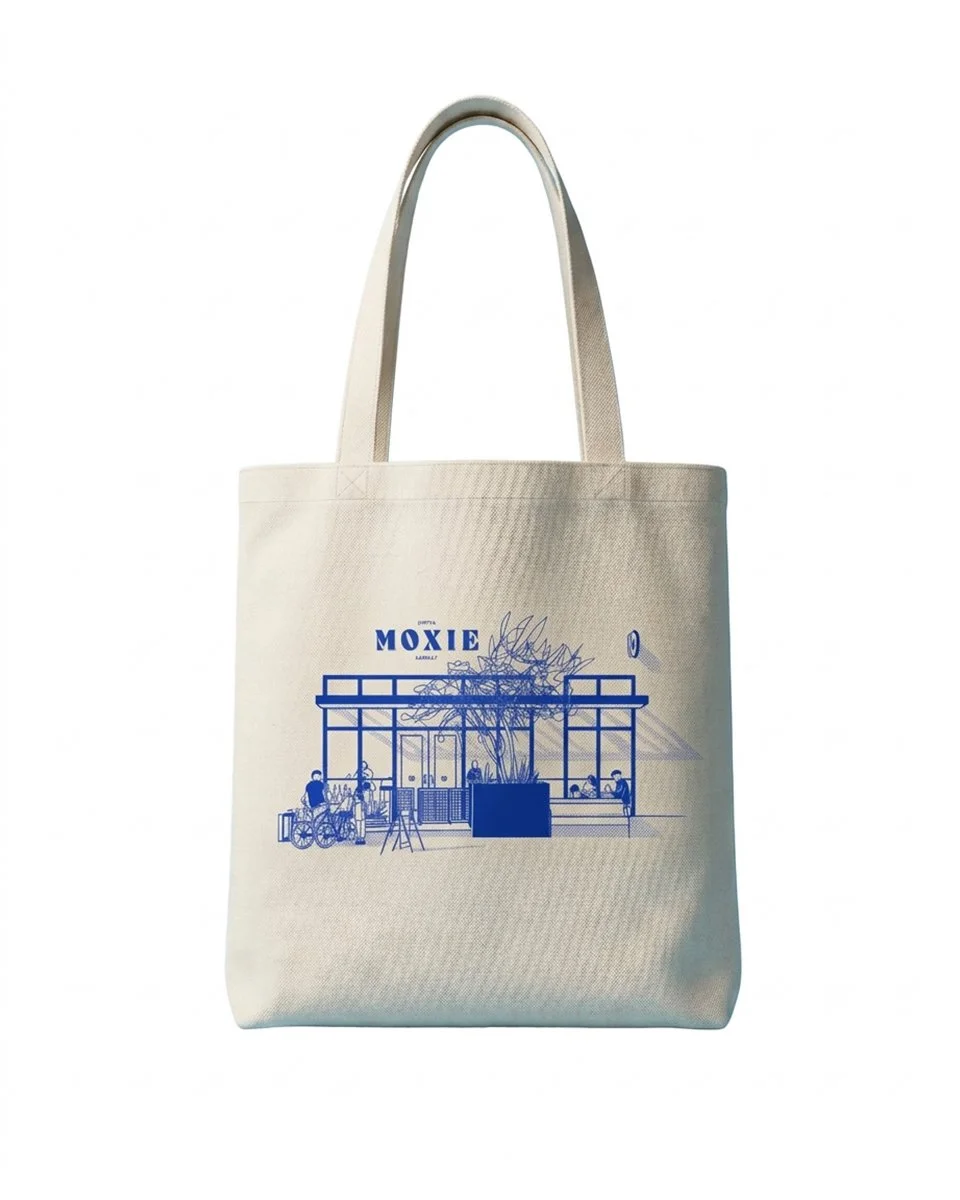 White canvas tote bag with blue MOXIE logo and storefront illustration