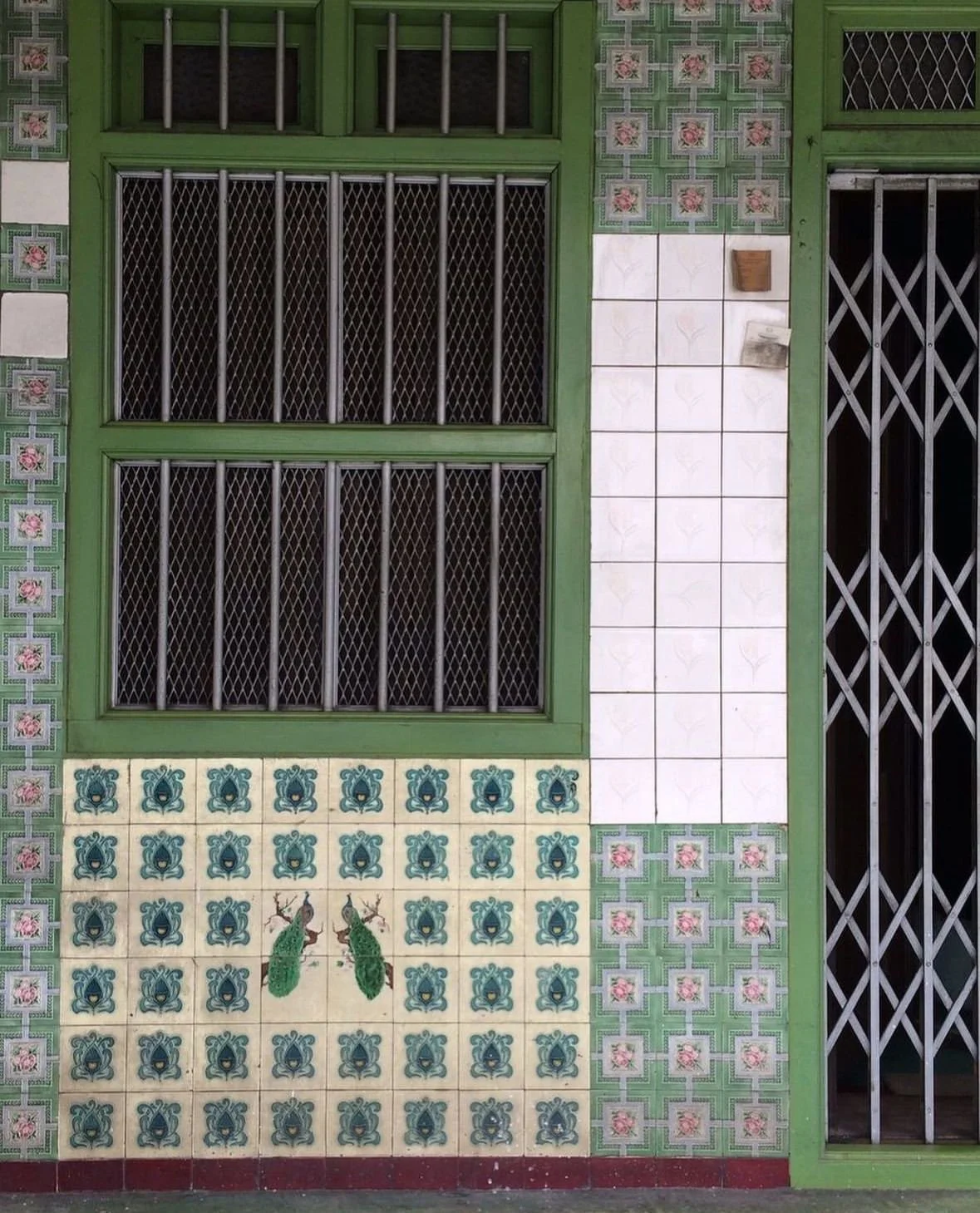 Ornate patterned tiles and peacock motifs on a traditional Southeast asian shophouse facade with green window frames.