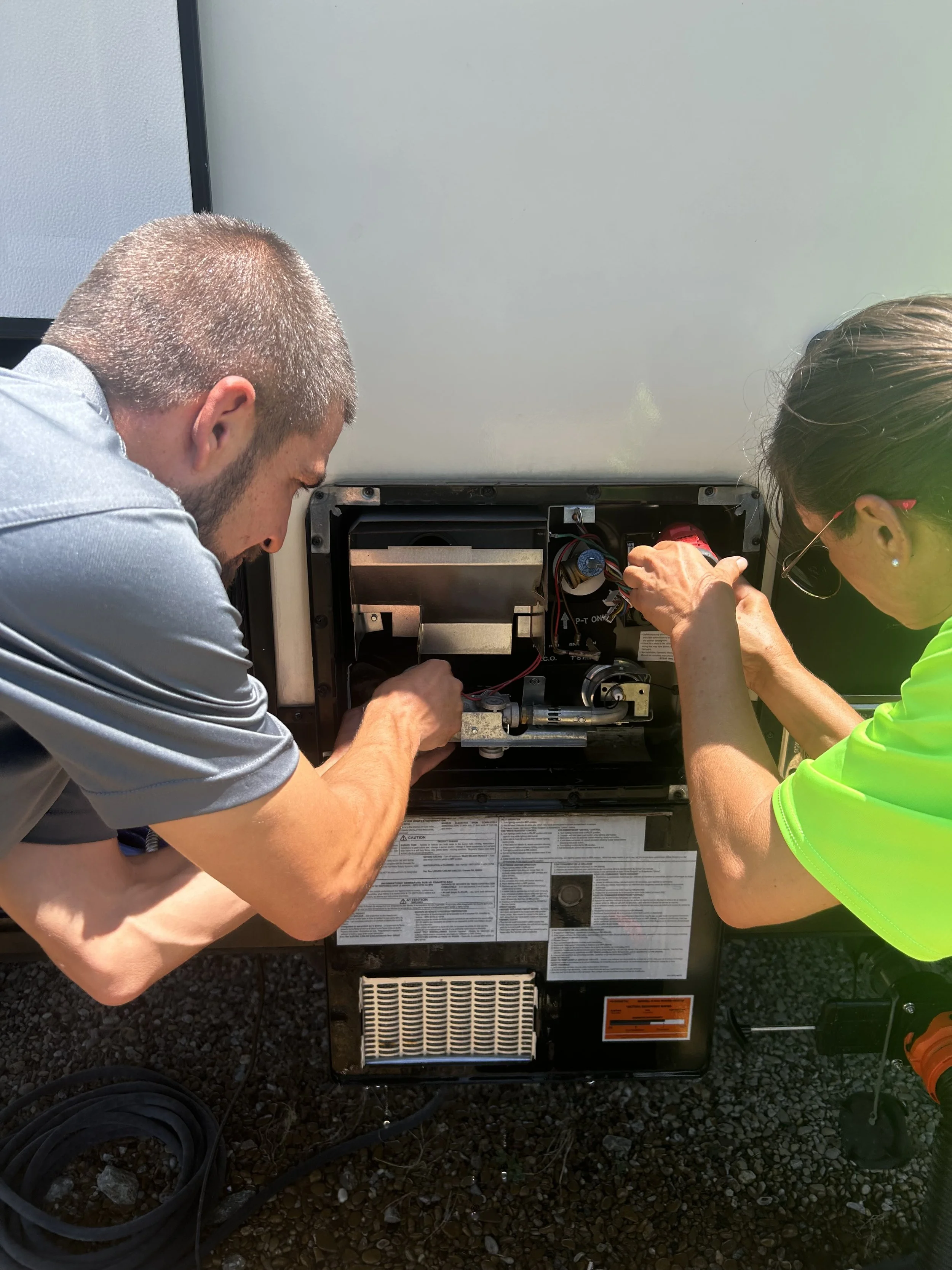 Two technicians repairing or inspecting a furnace or HVAC unit outdoors, with tools and equipment.
