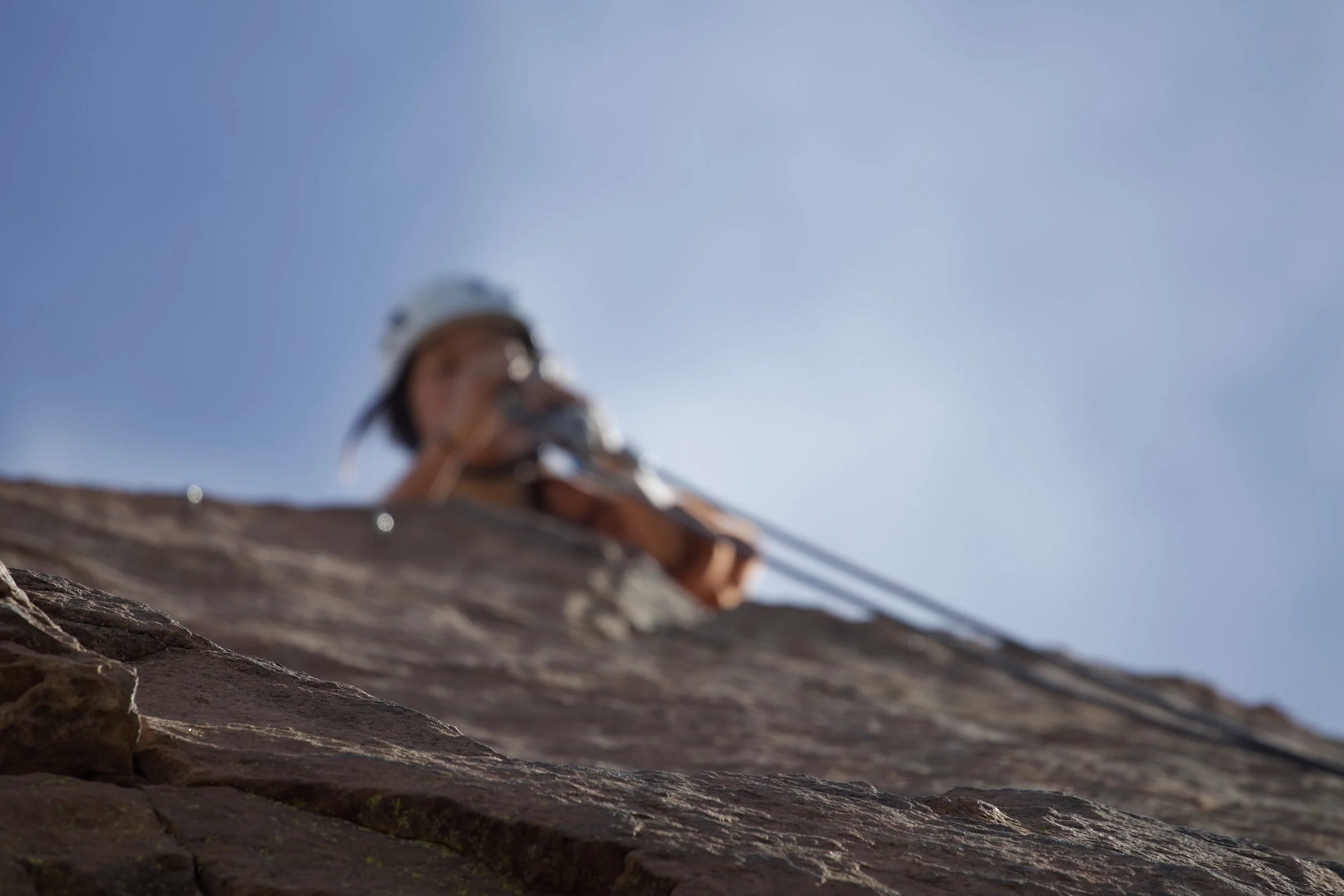"UP"
Rock climber with helmet ascending a rock face against a clear blue sky.