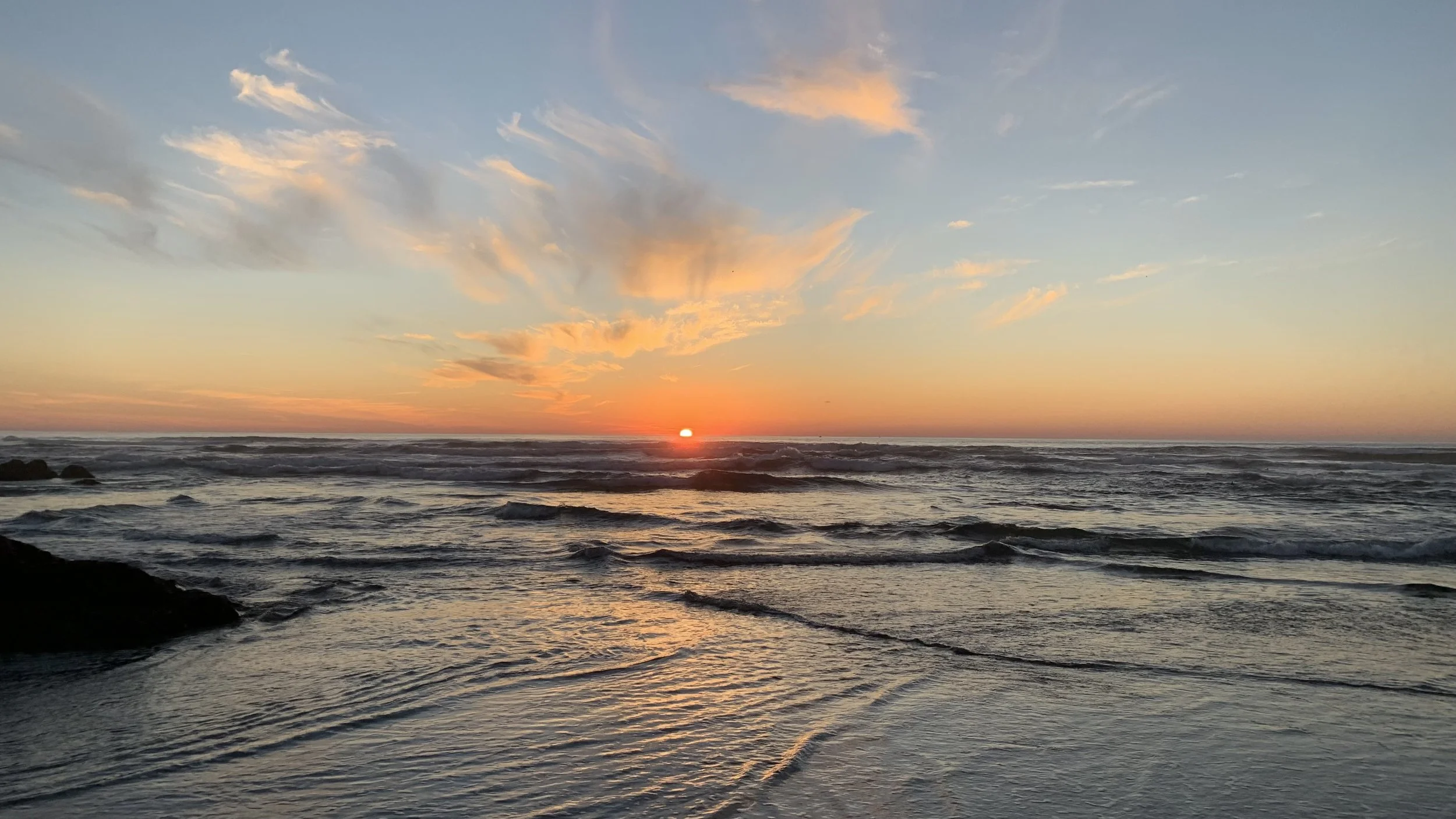 Sunset over the ocean with waves and colorful clouds in the sky.