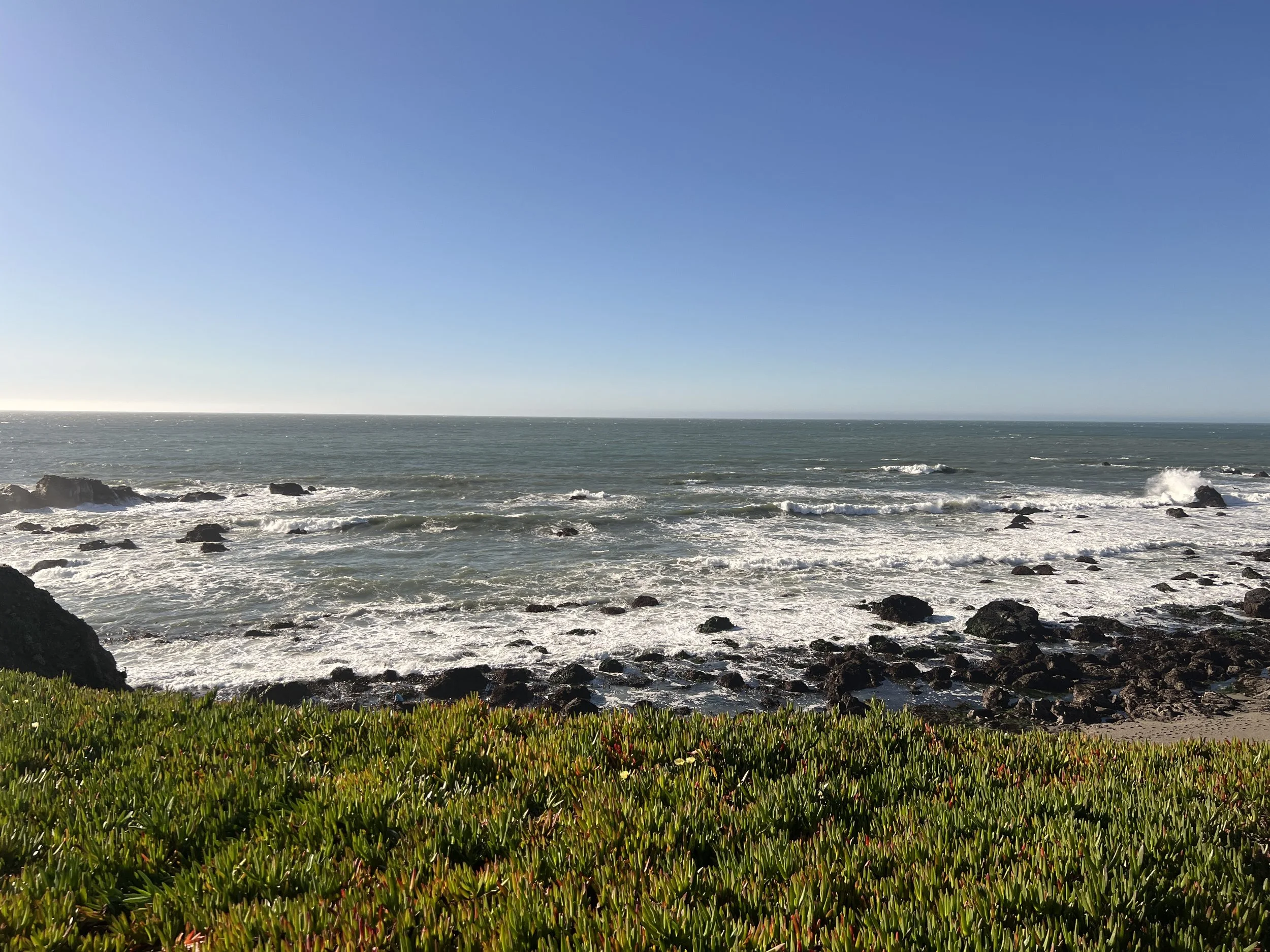 Coastal view with ocean waves and rocky shoreline under a clear blue sky.