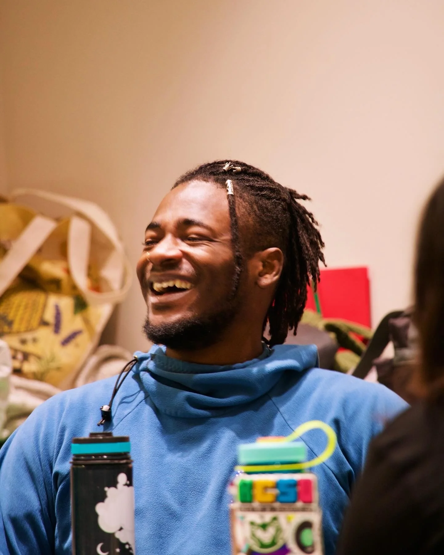 "All Smiles"
Person smiling while sitting in a casual setting with water bottles on the table.