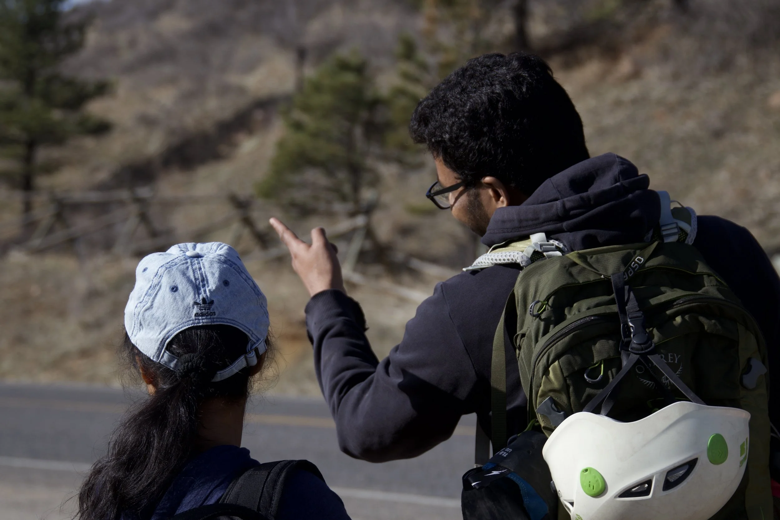 "Side by side"
Two people with backpacks and a helmet, in a natural outdoor setting, facing away from the camera.