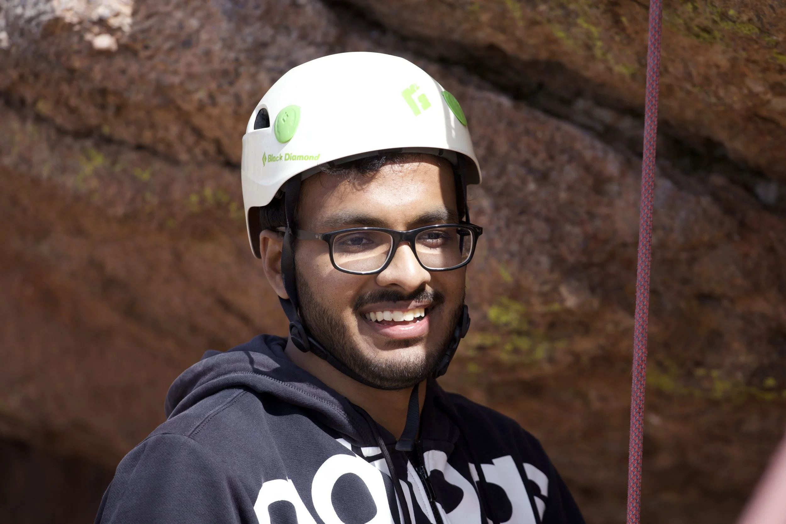 "adrenaline rush"
Person wearing a helmet and glasses outdoors, with climbing gear visible.