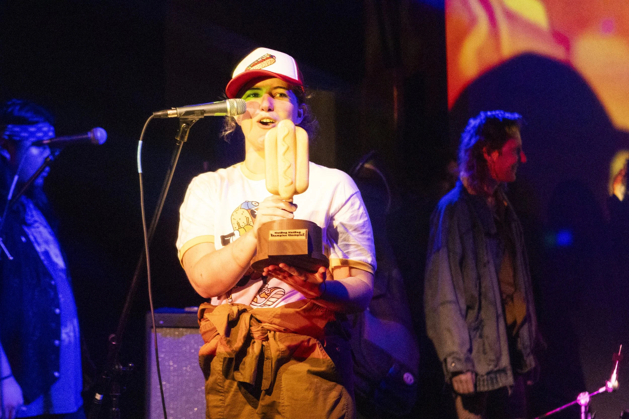 A young woman on stage holding an award shaped like a hot dog.