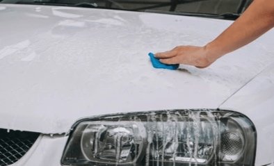 Person decontaminating a white car with a clay bar