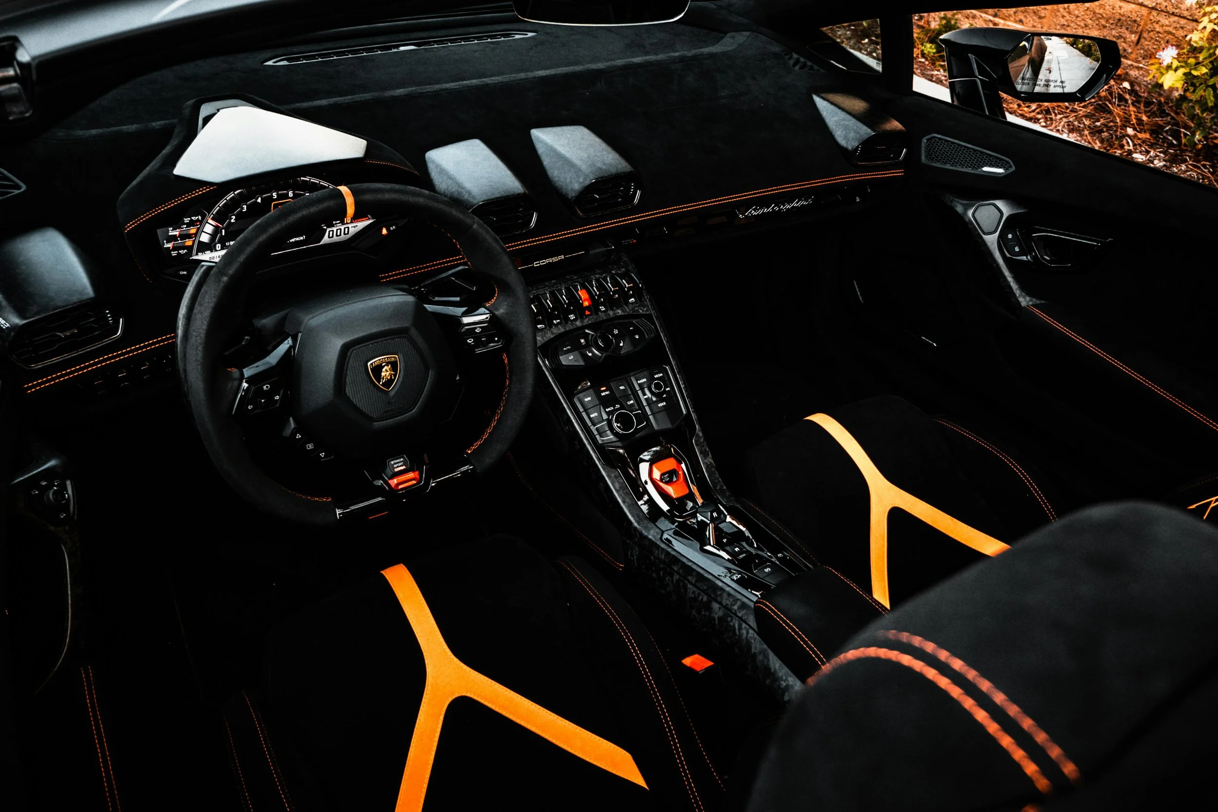 Luxury car interior with black and orange detailing, featuring a Lamborghini logo on the steering wheel, and a modern dashboard with controls.