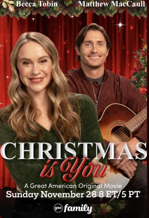 Poster of the movie "Christmas is You" featuring Becca Tobin and Matthew MacCaull, with Christmas decorations and red curtains in the background.