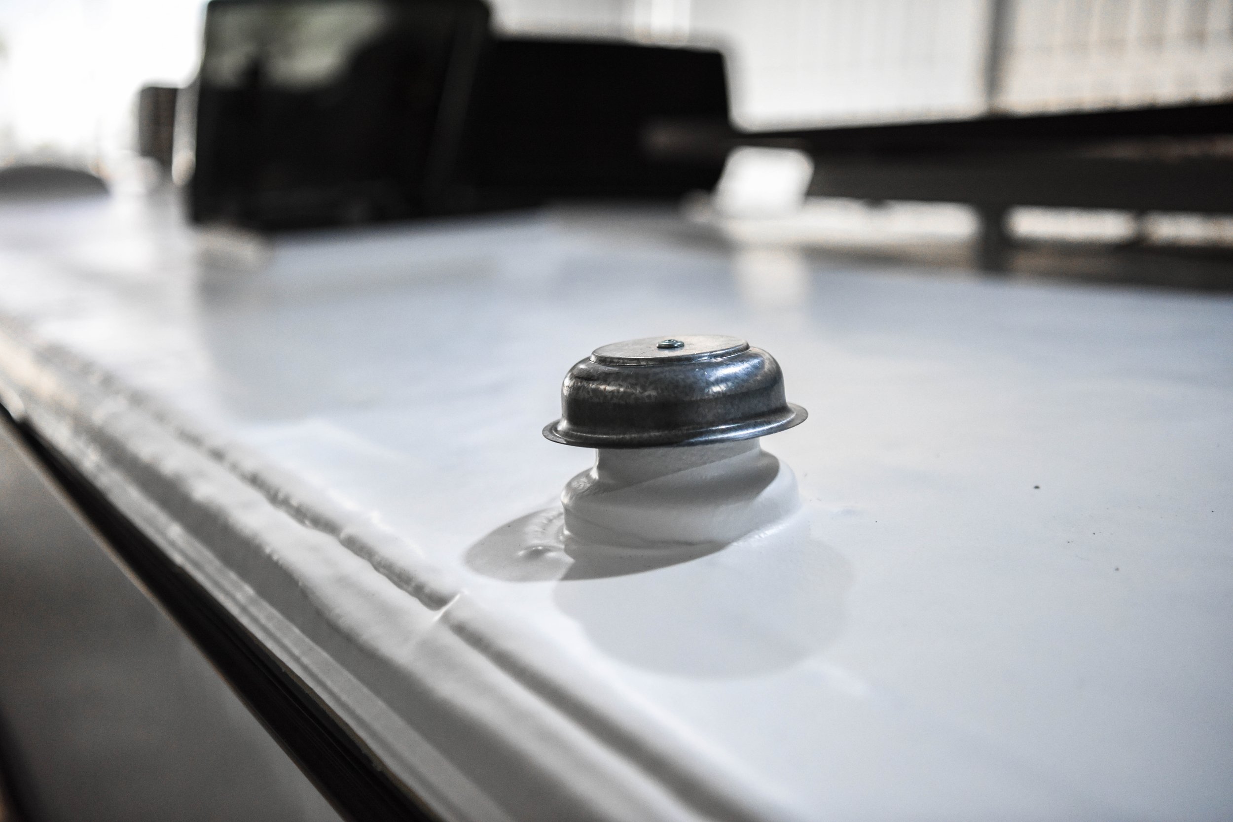 Close-up of a metal pluming vent on a Maxxseal Spray-On Roof, with an A/C in the blurry background.