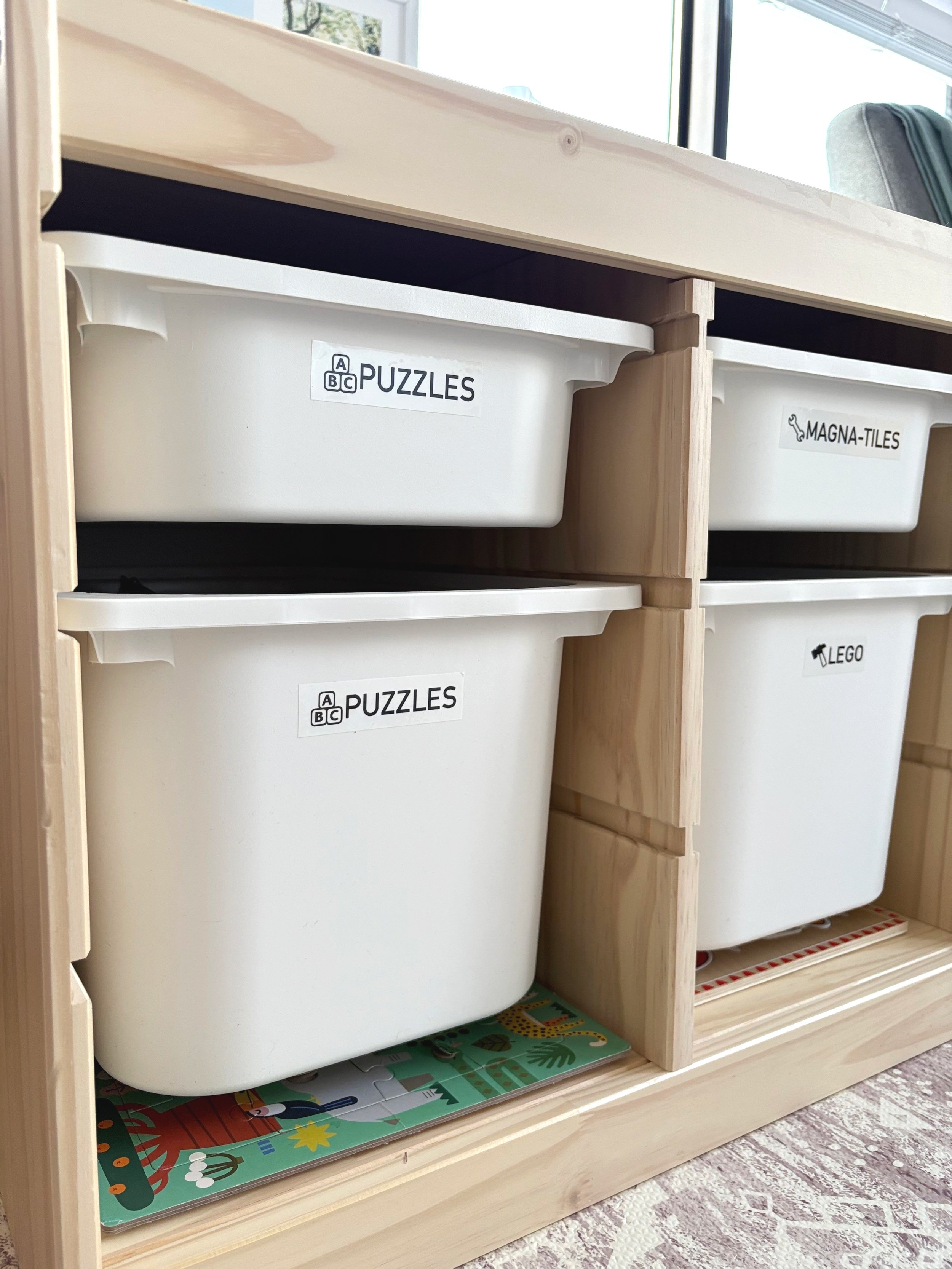 Neatly organized and labeled toy storage bins with the words puzzles, Magna-tiles and Lego