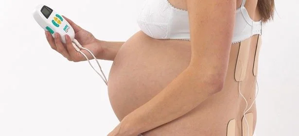 Pregnant woman lying with electrodes attached to her abdomen and holding a fetal Doppler device, used for monitoring the baby's heartbeat.