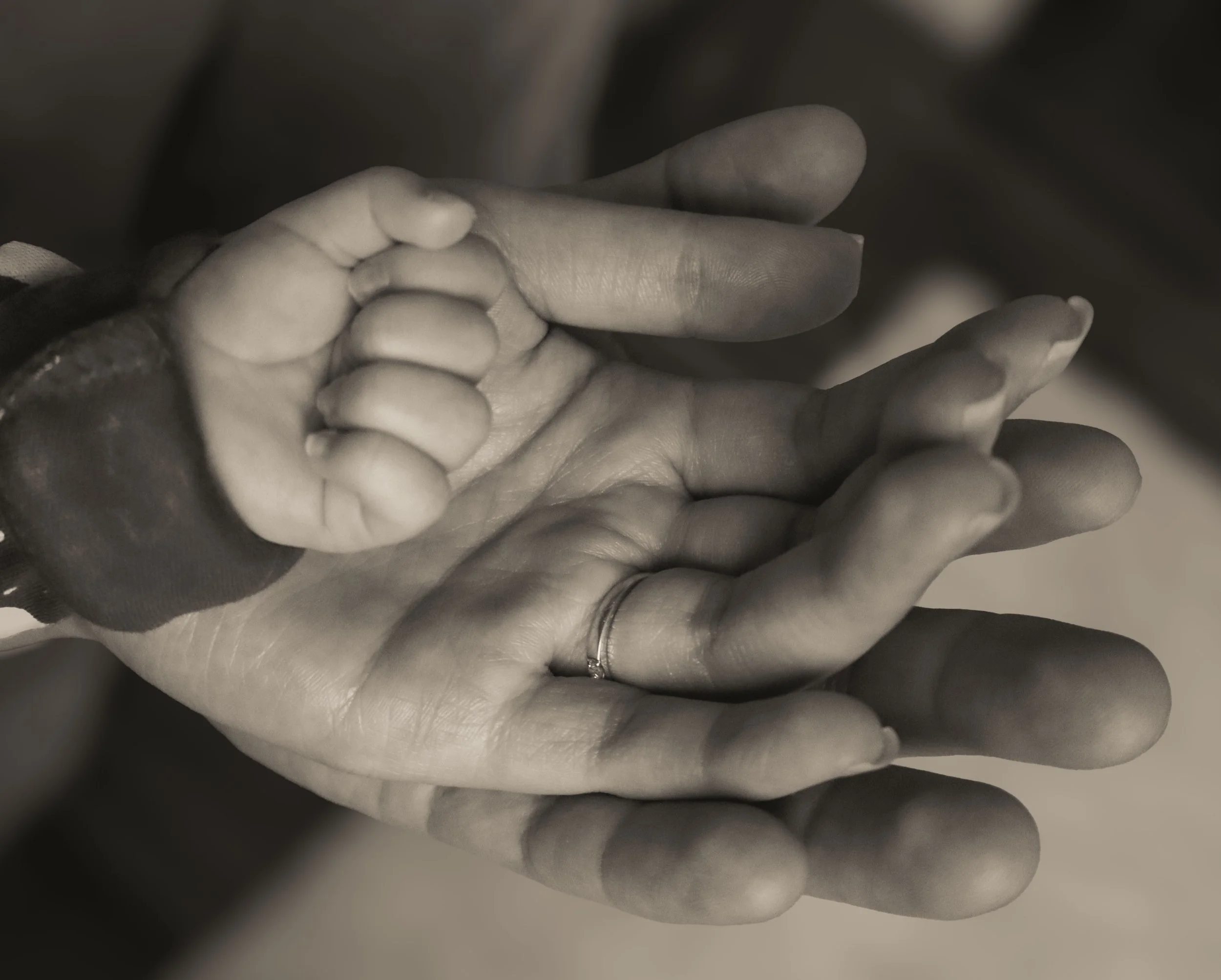 A close-up of a small child's hand grasping an adult's finger, both hands shown in black and white.