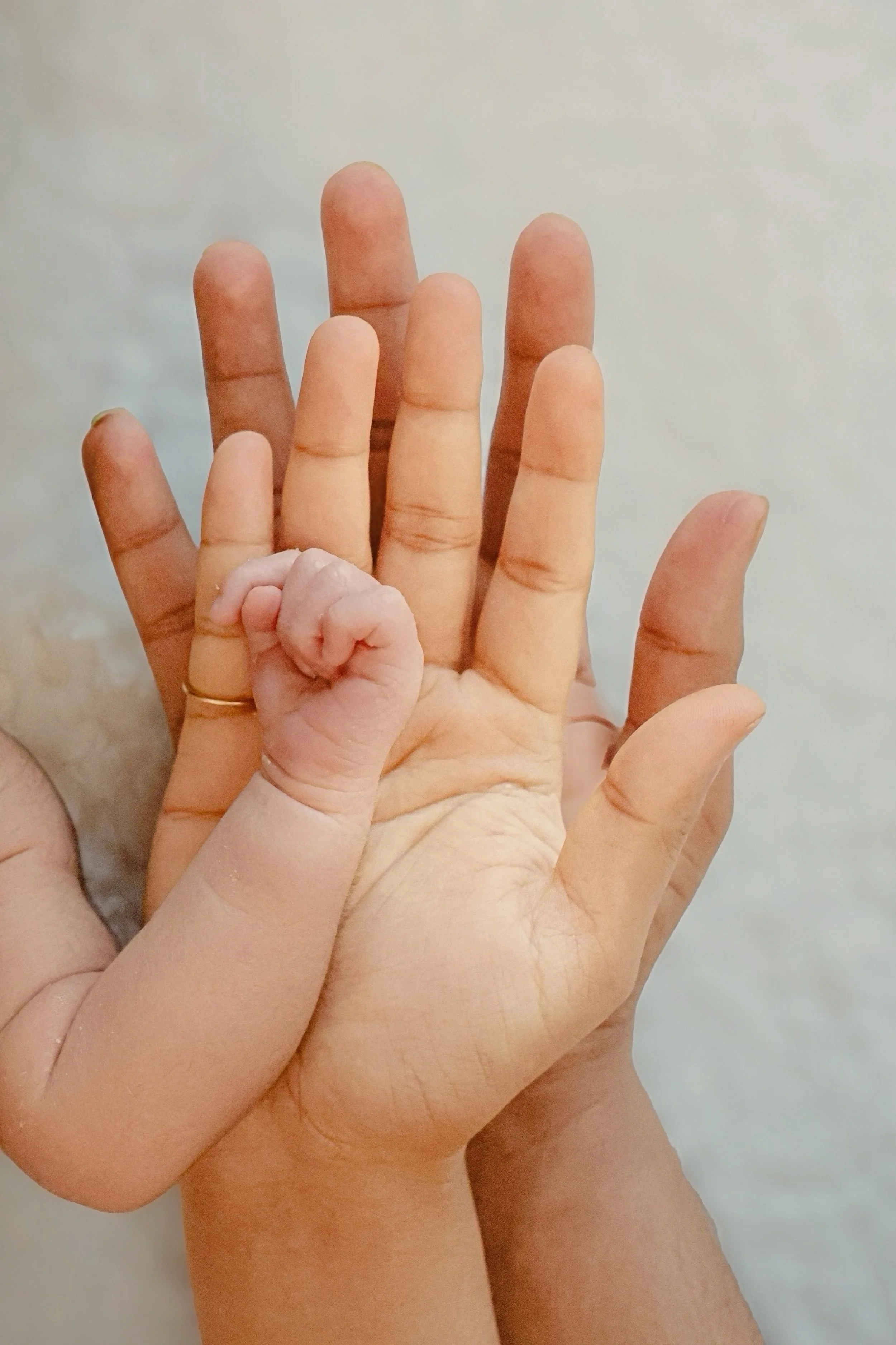 A small infant's hand is grasped by an adult's hand, shown in a close-up shot.