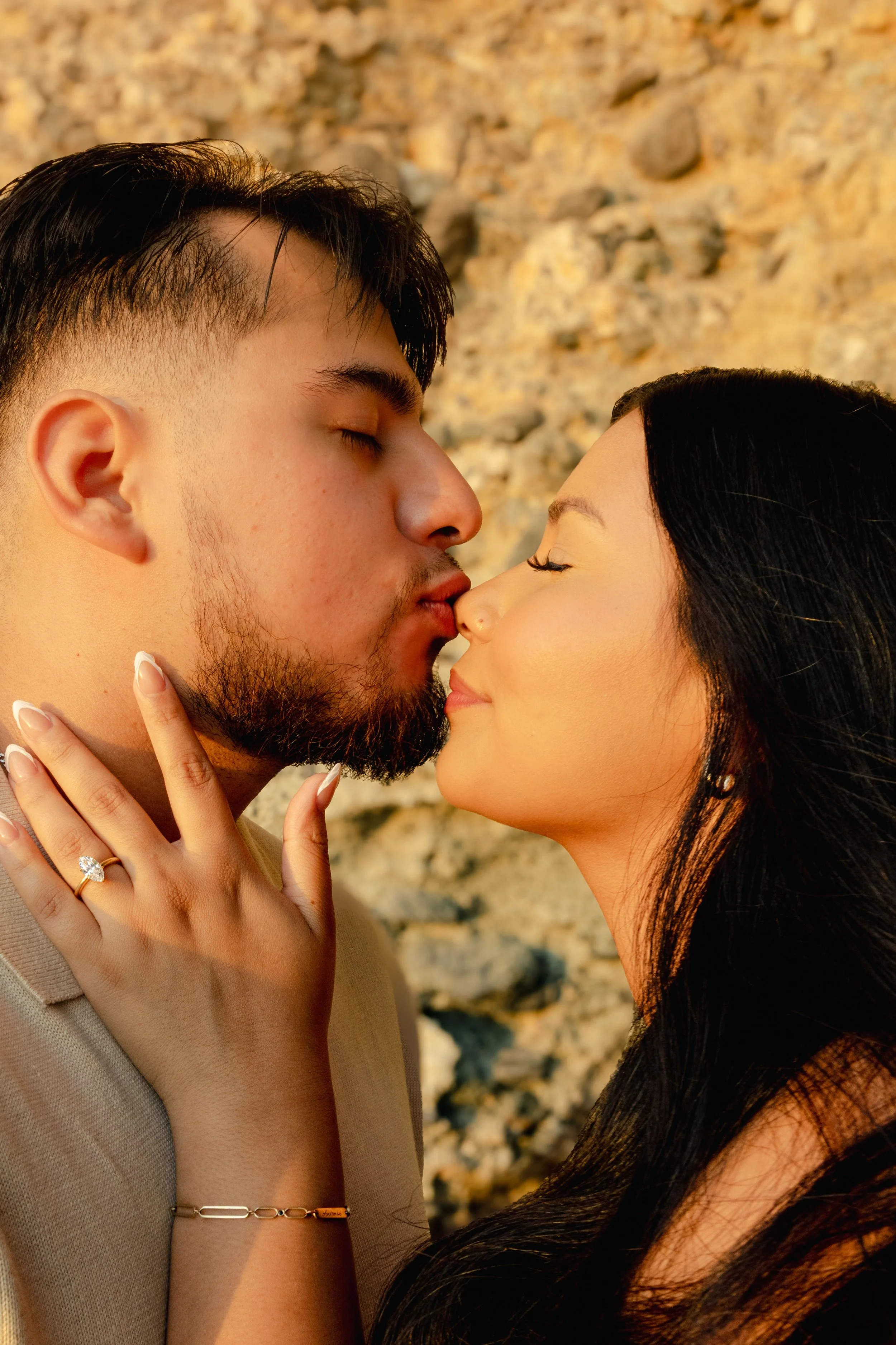 A couple about to kiss, with the man's eyes closed and the woman's face tilted up, against a rocky background.