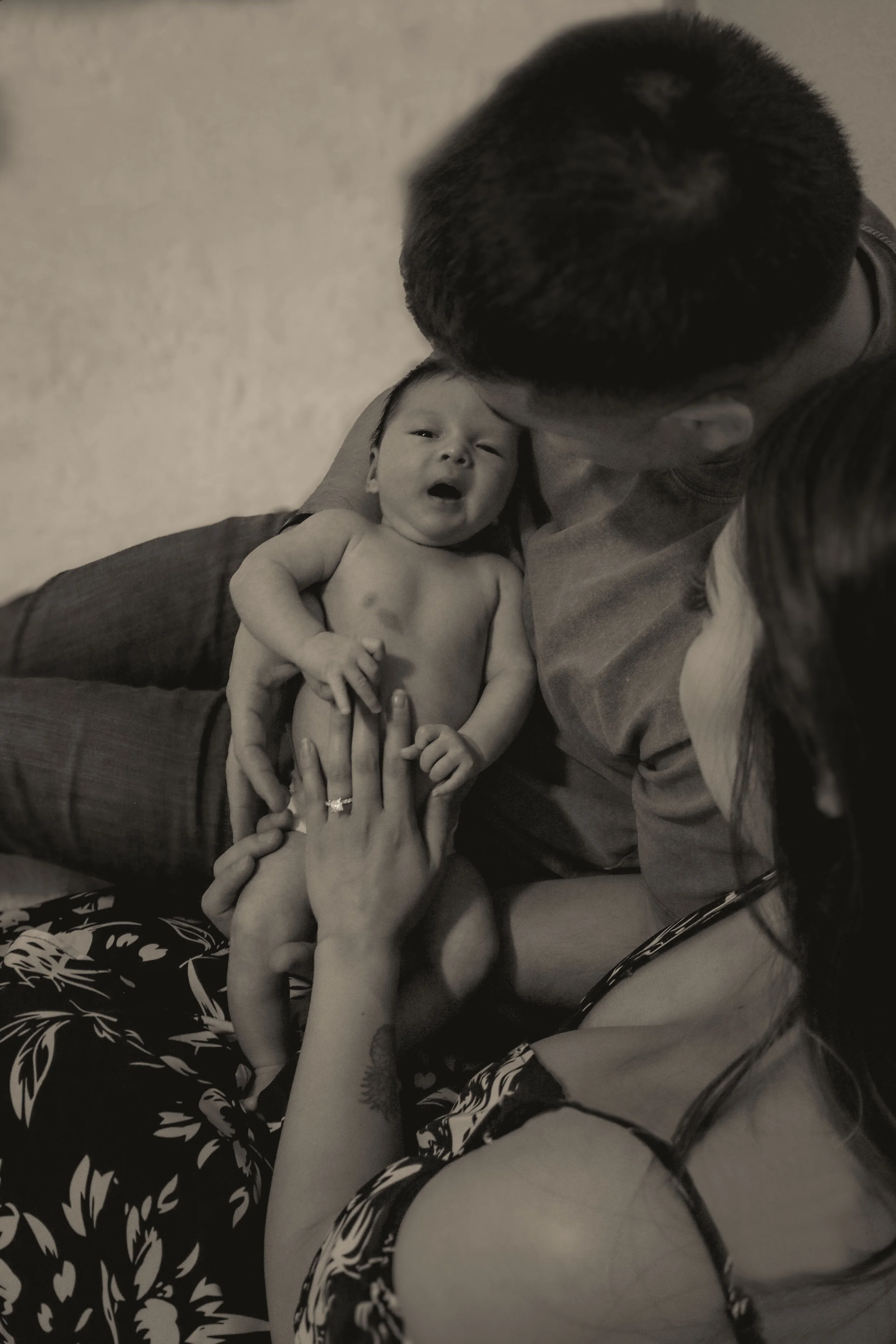 A family gathering with a man, woman, and baby, where the woman is holding the baby and the man is leaning in close, all focused on the baby.