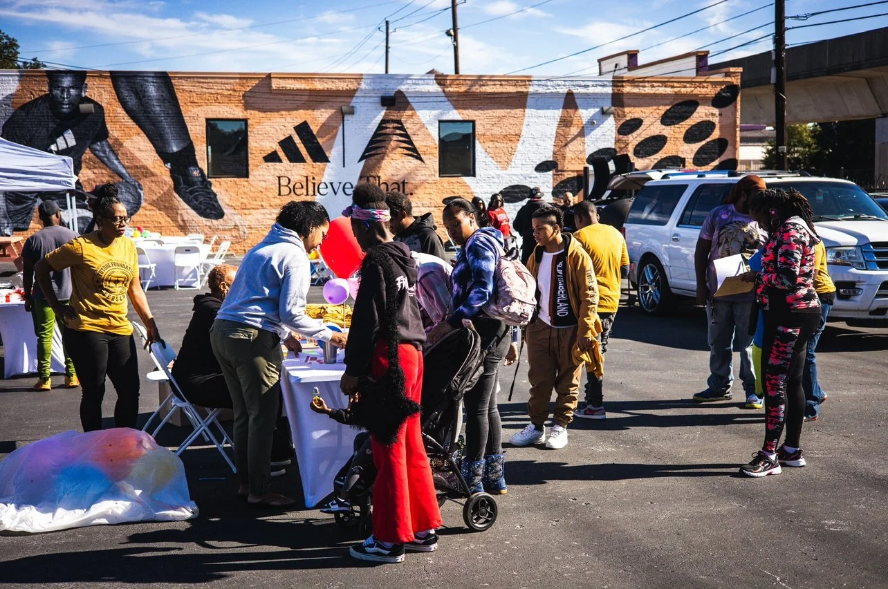 People gathering at an outdoor event with tables and decorations, near a mural.