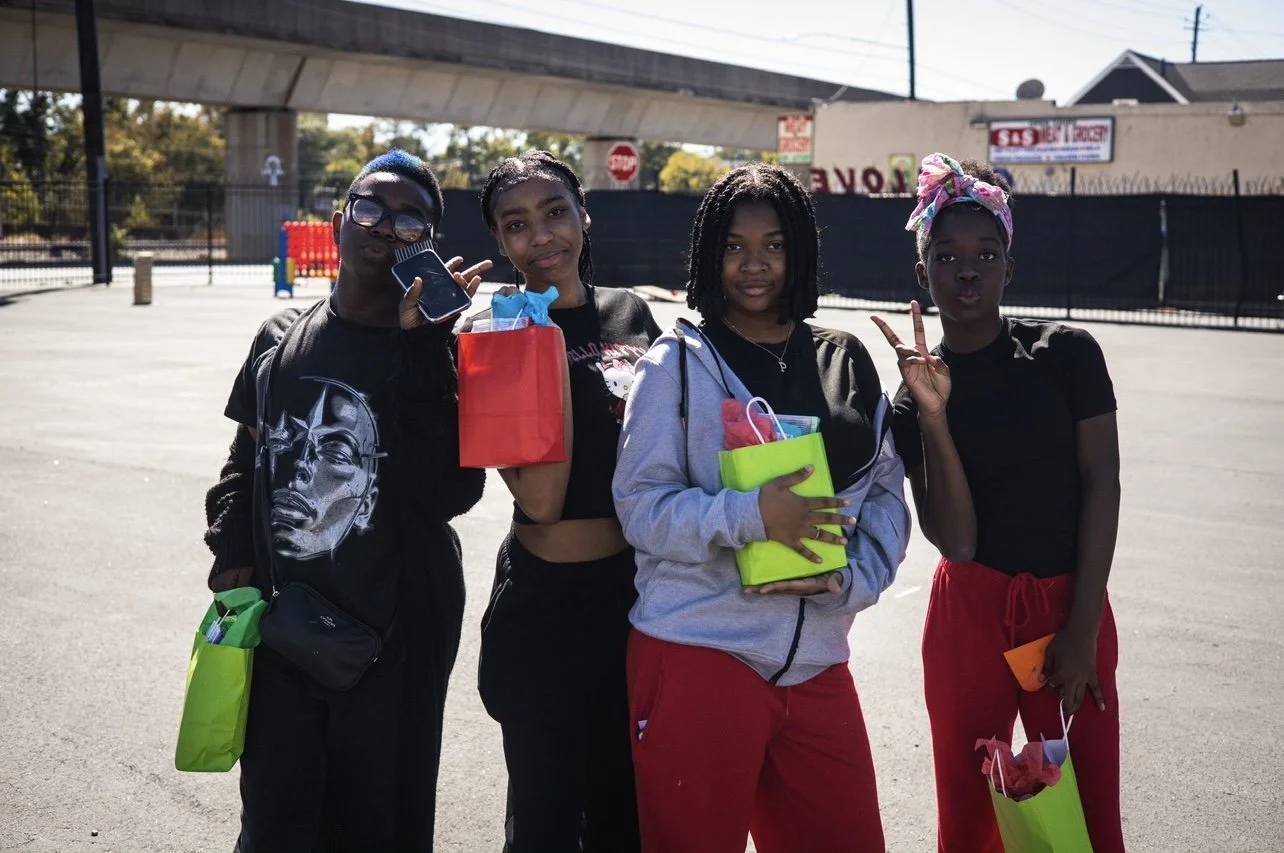 Four people standing outdoors with gift bags, smiling and posing for the camera.