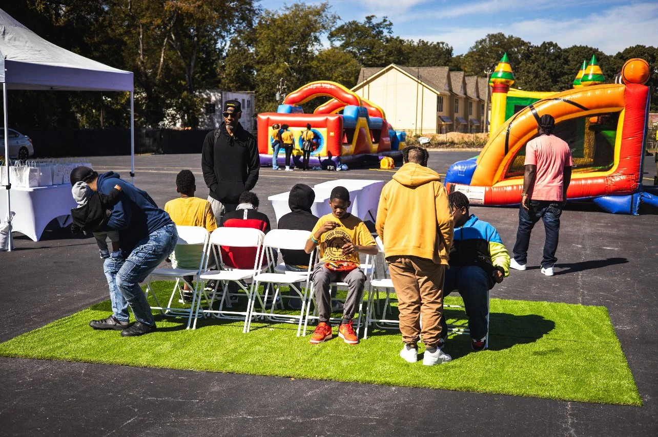 Outdoor event with people sitting on chairs, inflatable bounce houses, and a canopy.